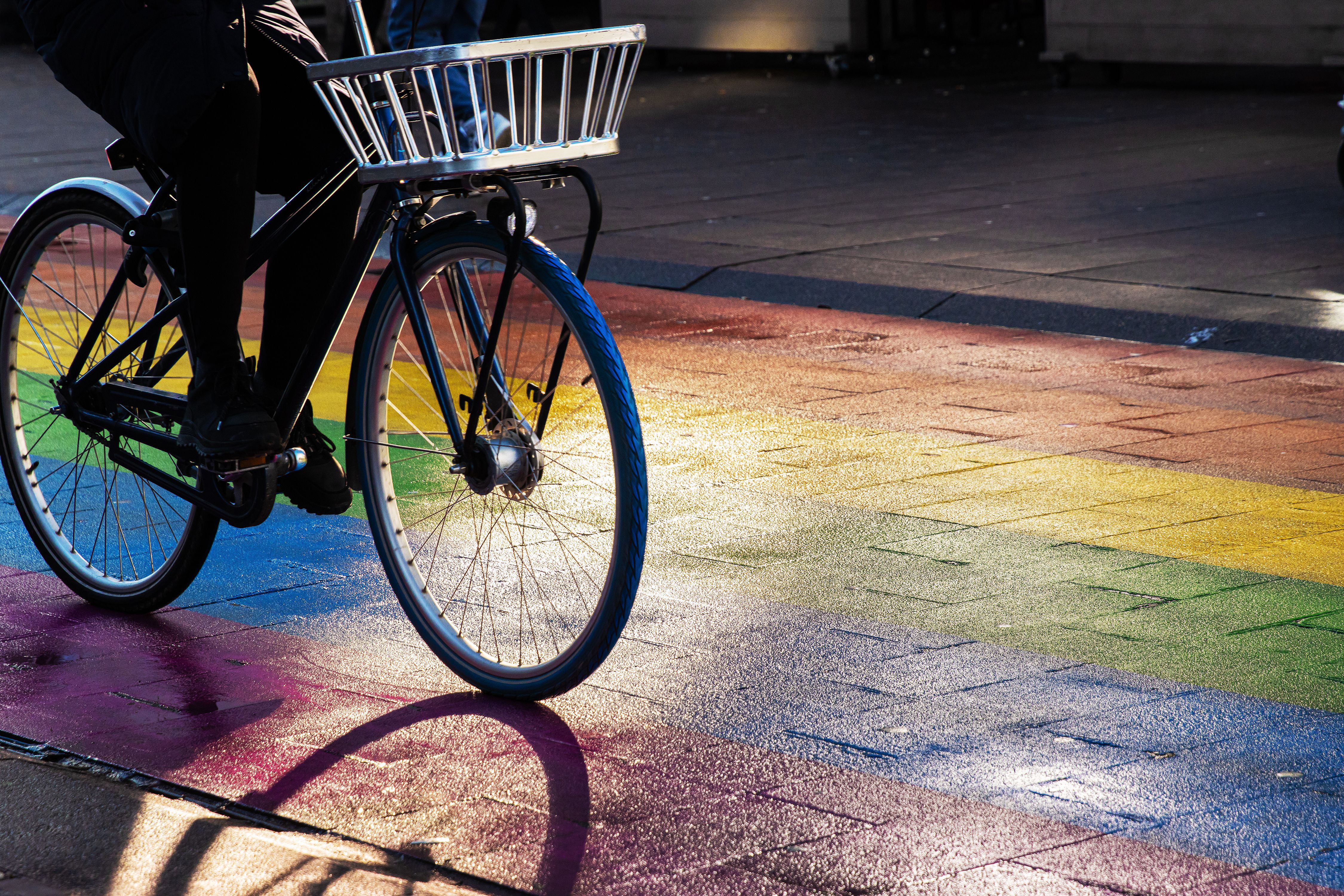 Cyclist riding a bicycle with a metal front basket on a rainbow street. Regenboogvlag in the Grote Marktstraat in the center of the Hague, Netherlands. Selective focus. Movement effect