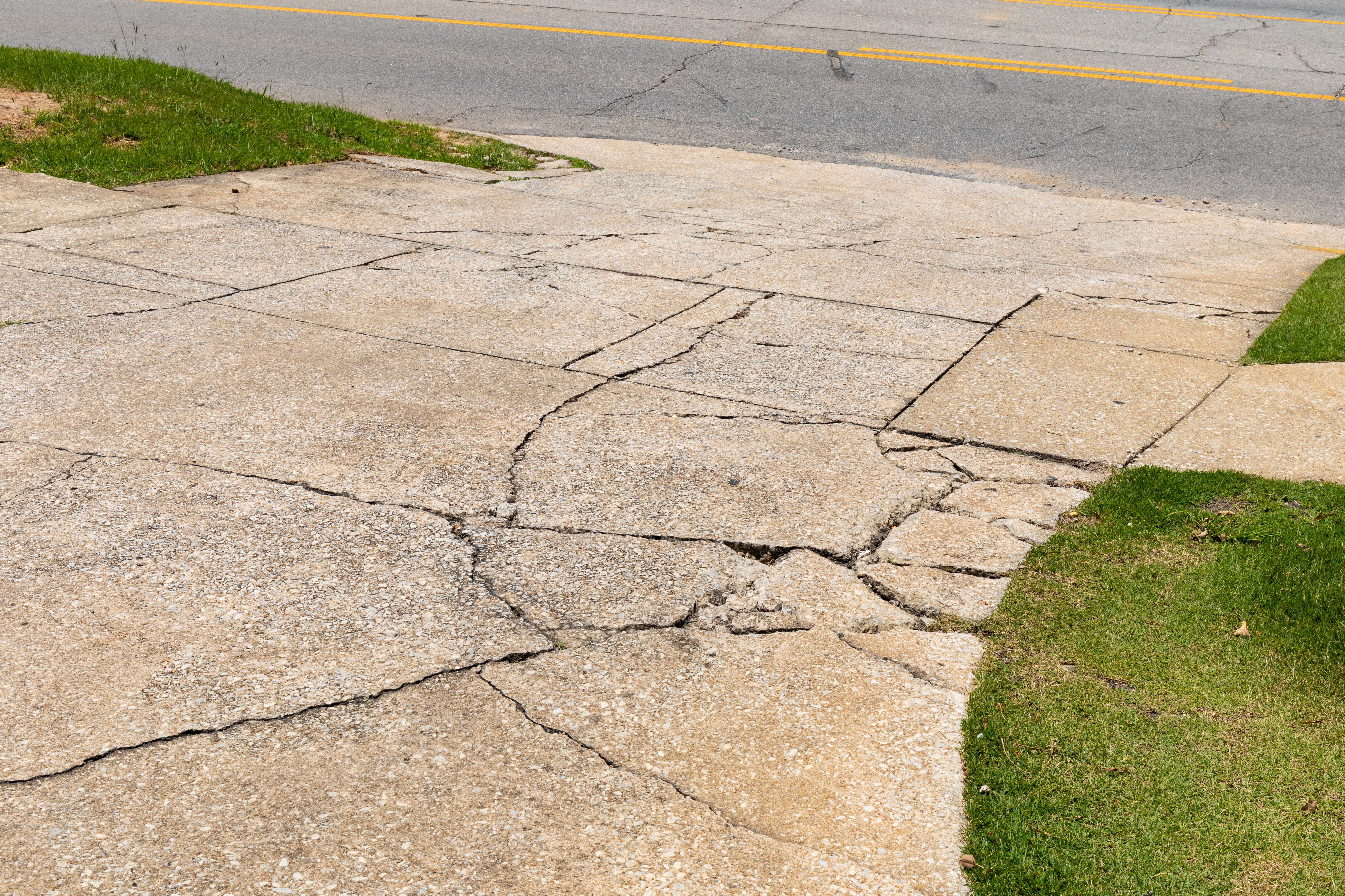 Cracked and broken aggregate concrete driveway descending into an asphalt roadway, flanked by green grassy areas, creative copy space Cracked and broken aggregate concrete driveway descending into an asphalt roadway, flanked by green grassy areas, creative copy space