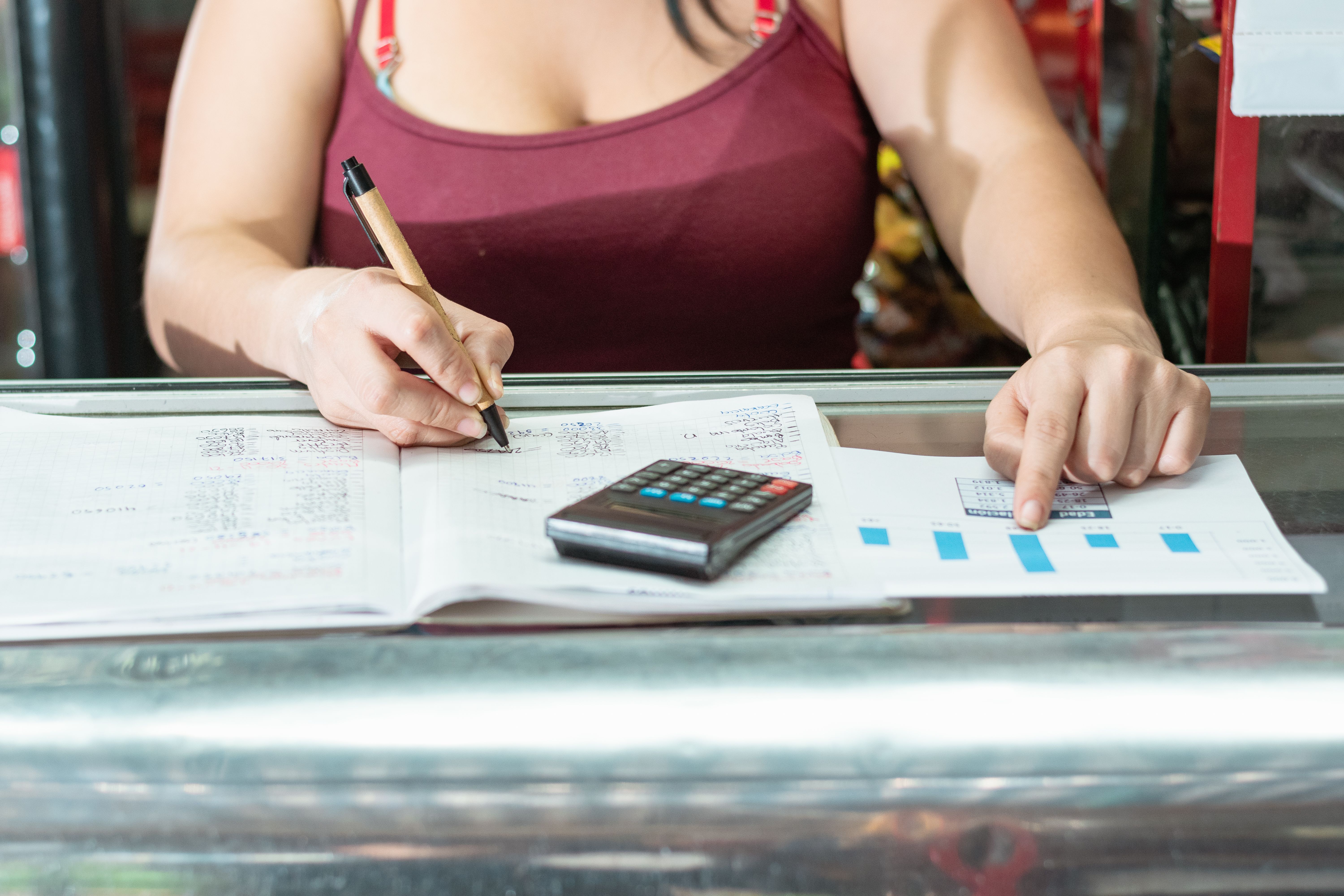 la mano de una niña señalando su gráfico de estadísticas comerciales. escribir con un bolígrafo de cartón ecológico y una pequeña calculadora negra en un cuaderno grande. hacer un balance de ventas.