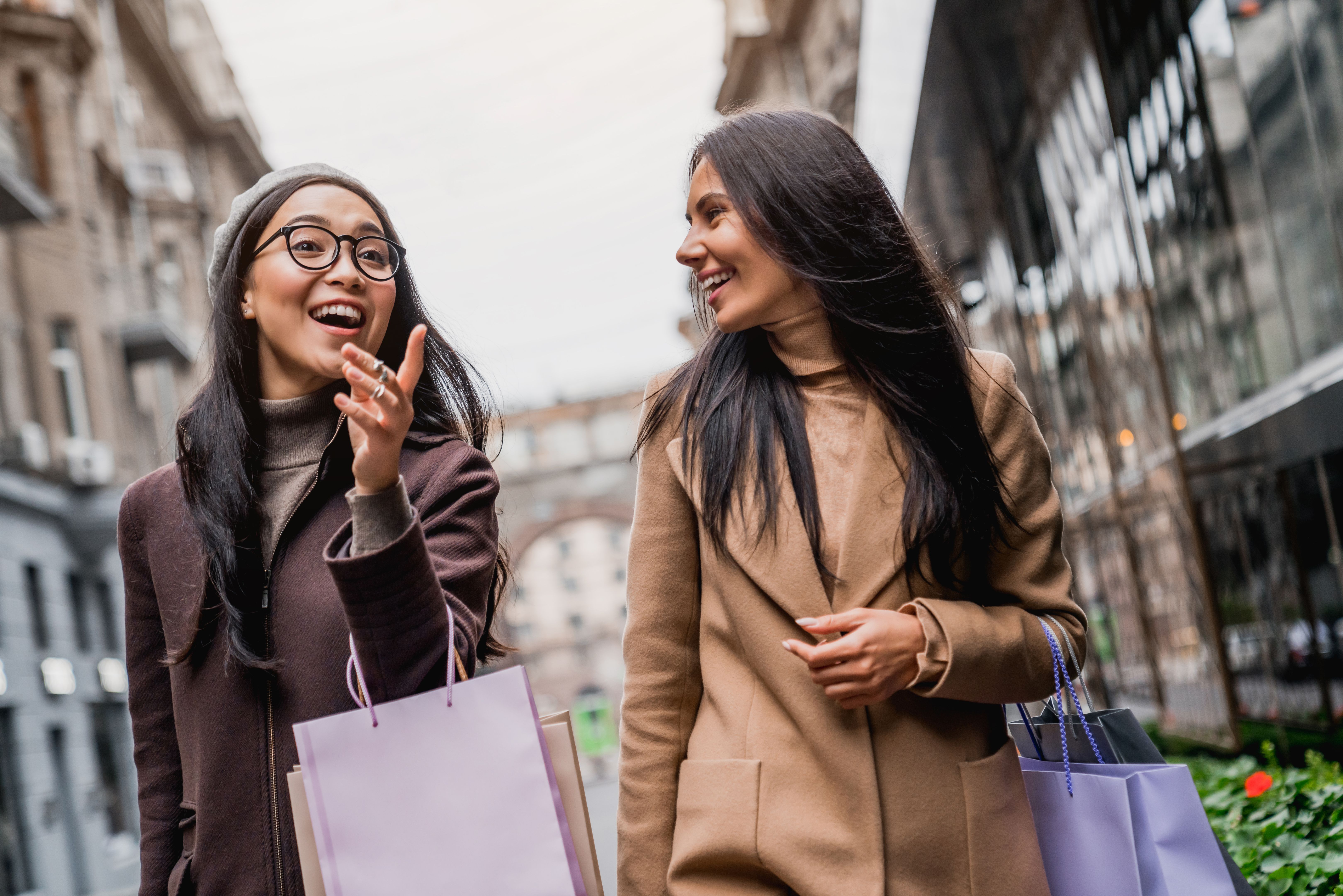 Portrait of two happy women with shopping bags pointing while walking together on the city streets