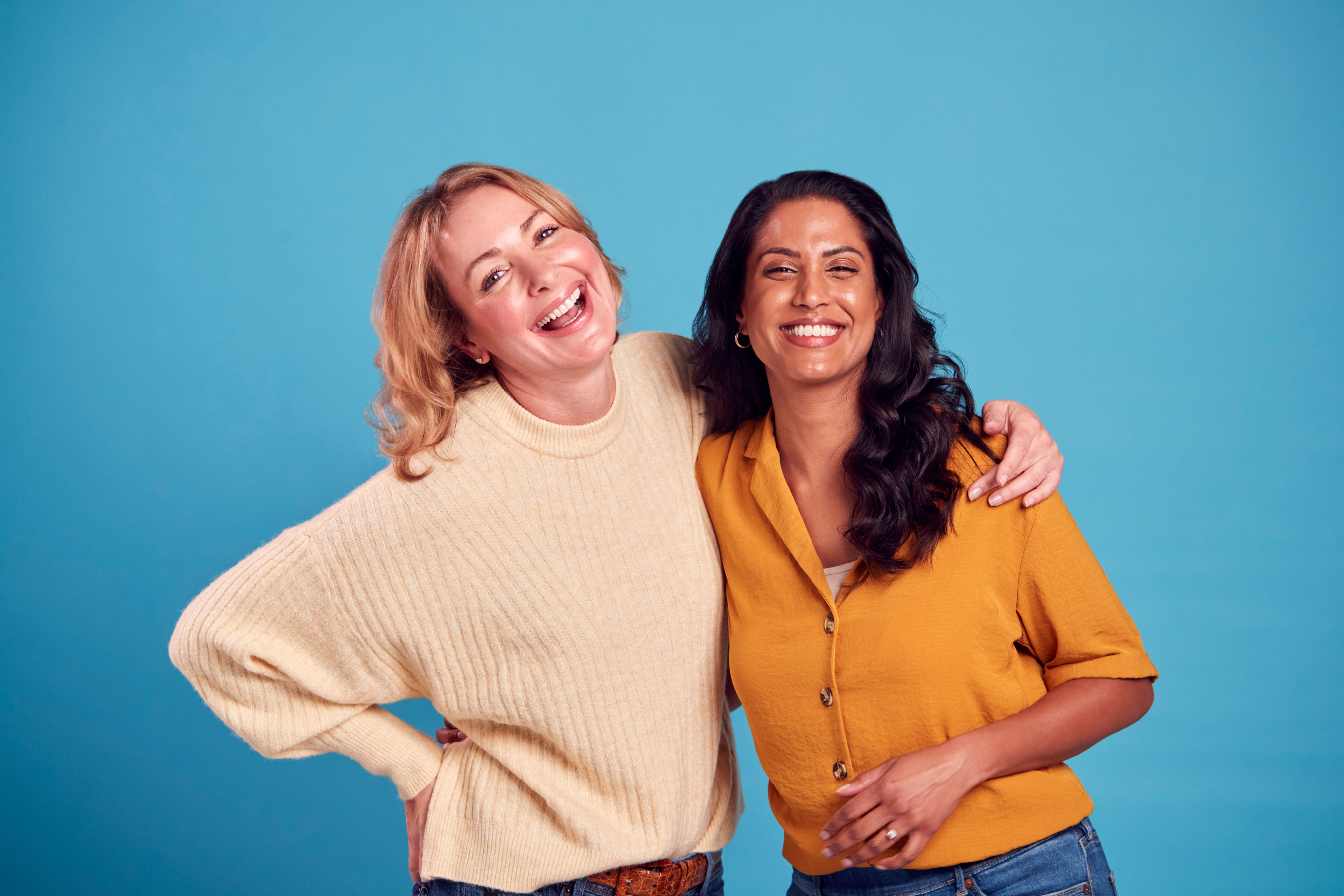 Portrait Of Two Mature Female Friends Laughing At Camera Against Blue Background Portrait Of Two Mature Female Friends Laughing At Camera Against Blue Background