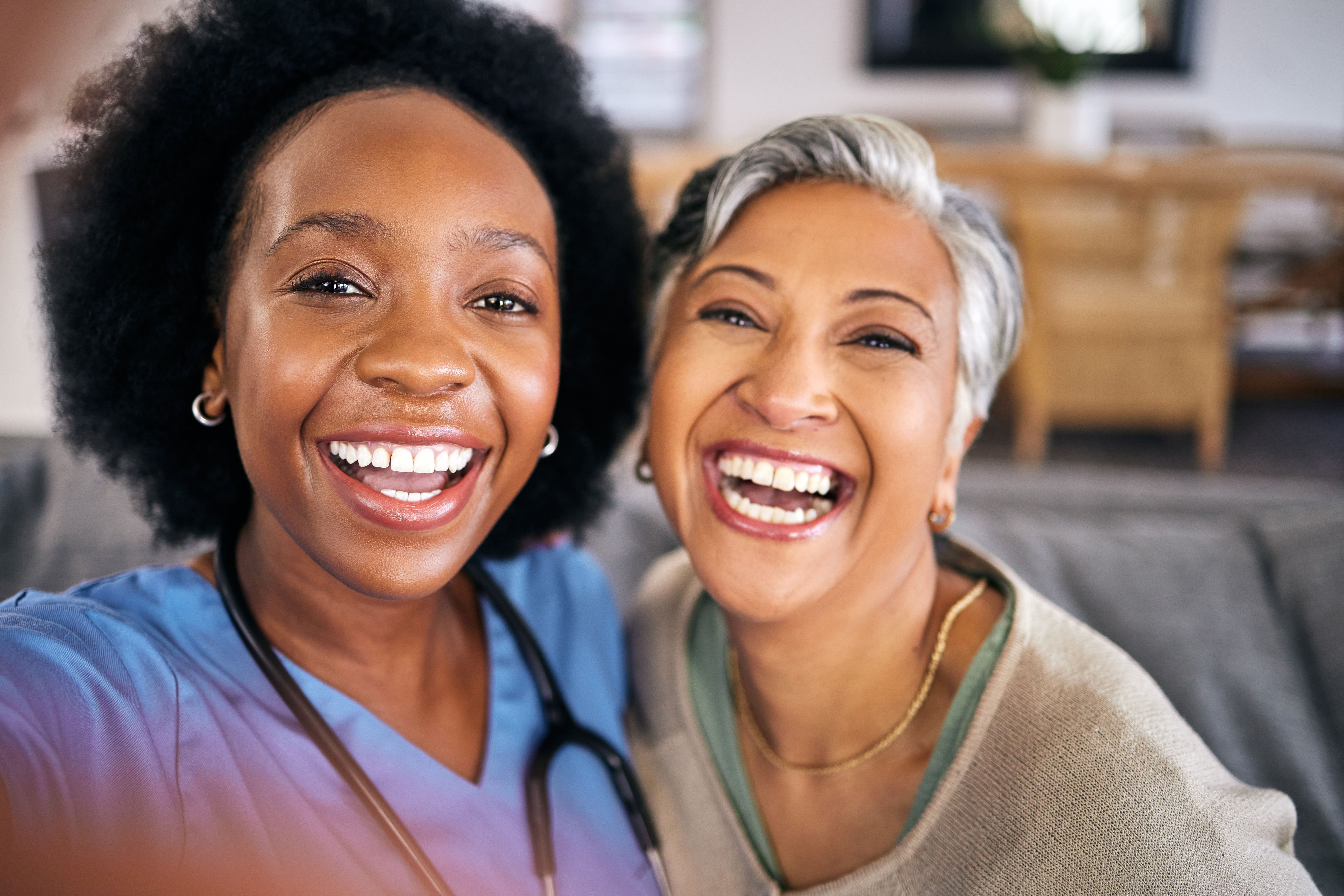 Selfie, face and assisted living caregiver with an old woman in the living room of a home together. Portrait, smile or support with a happy nurse or medical volunteer and senior patient in a house