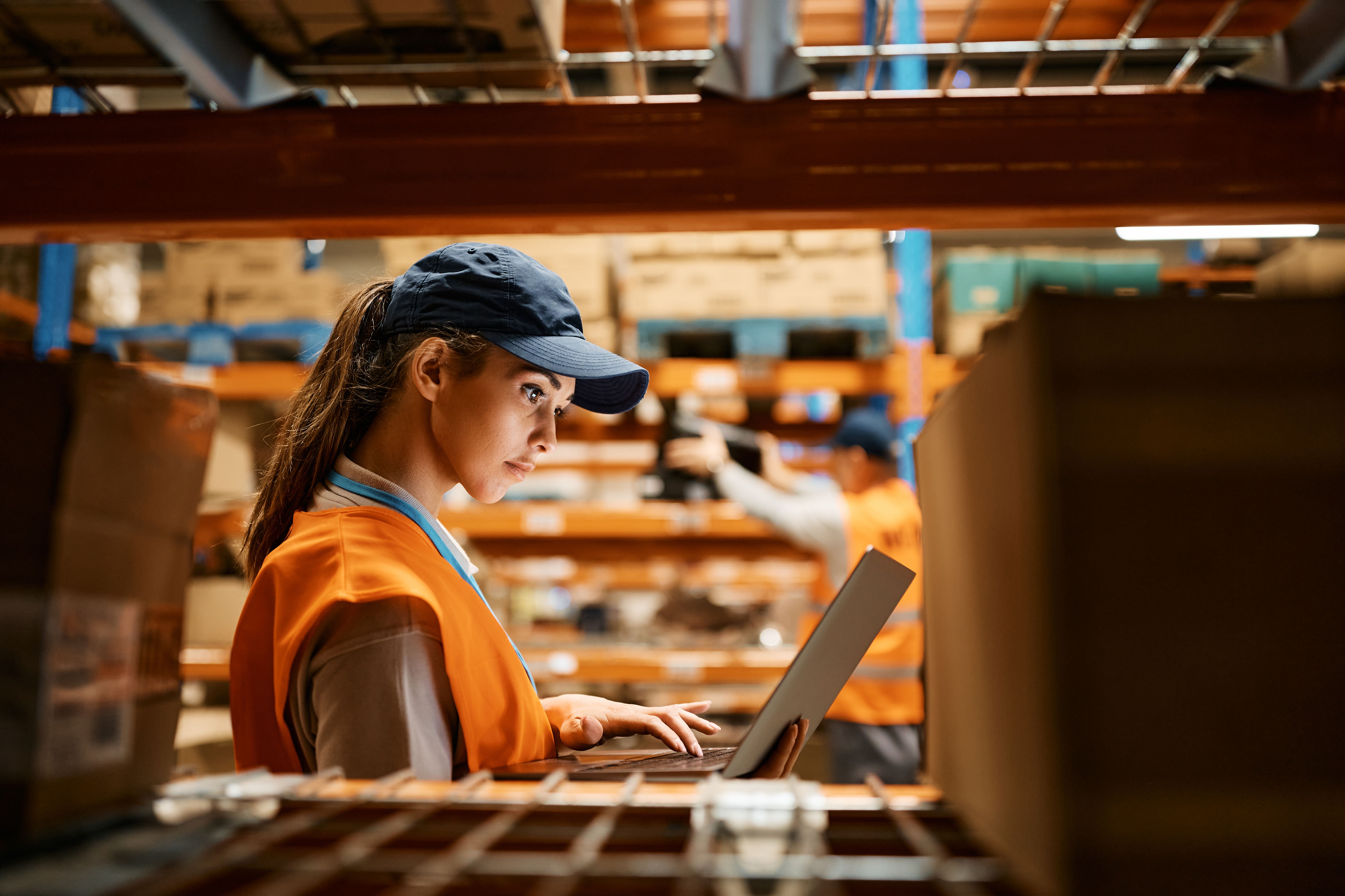 Female worker using laptop while working at distribution warehouse.