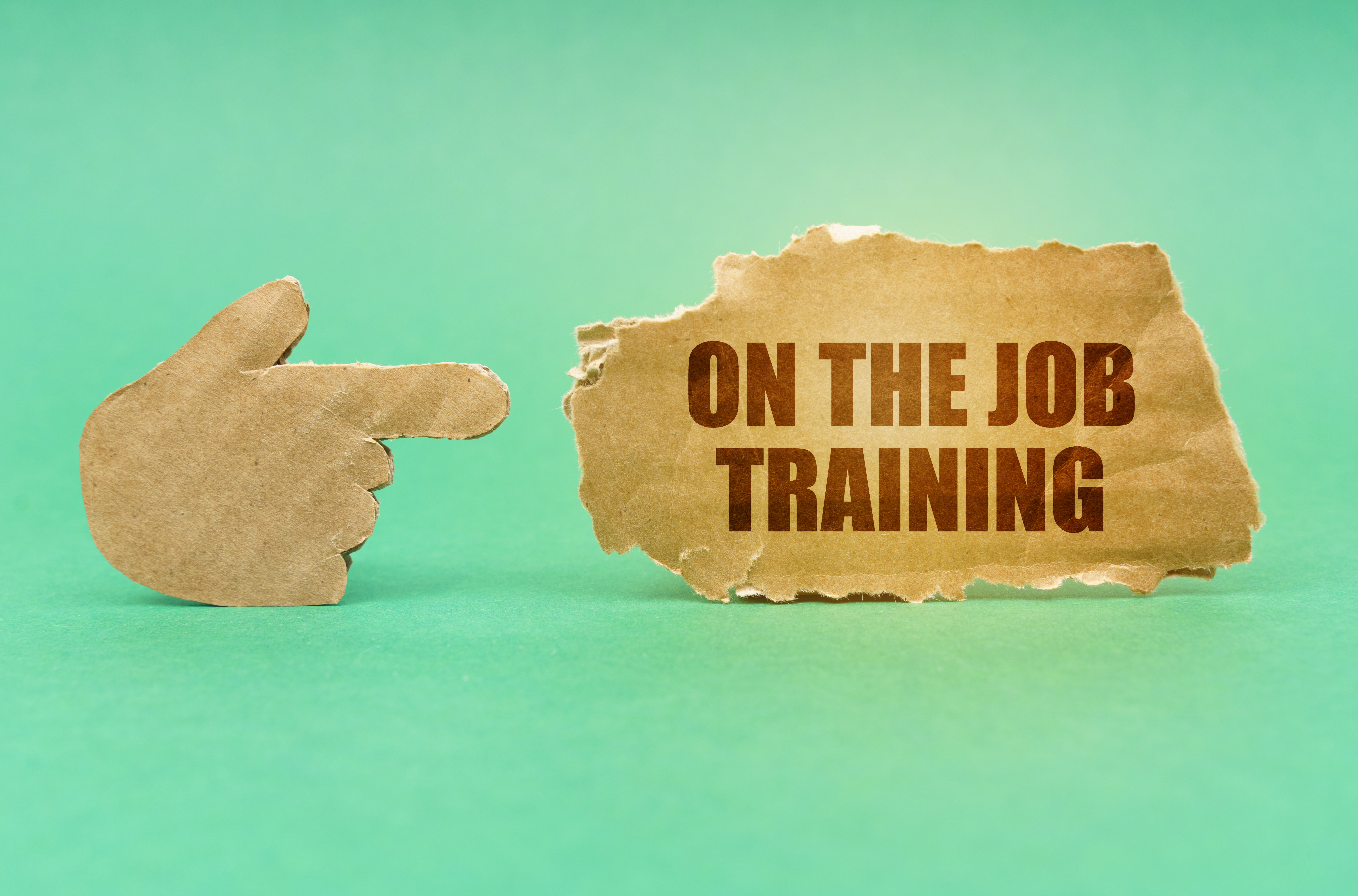 On a green surface, a cardboard hand points to a sign with the inscription - On the Job Training