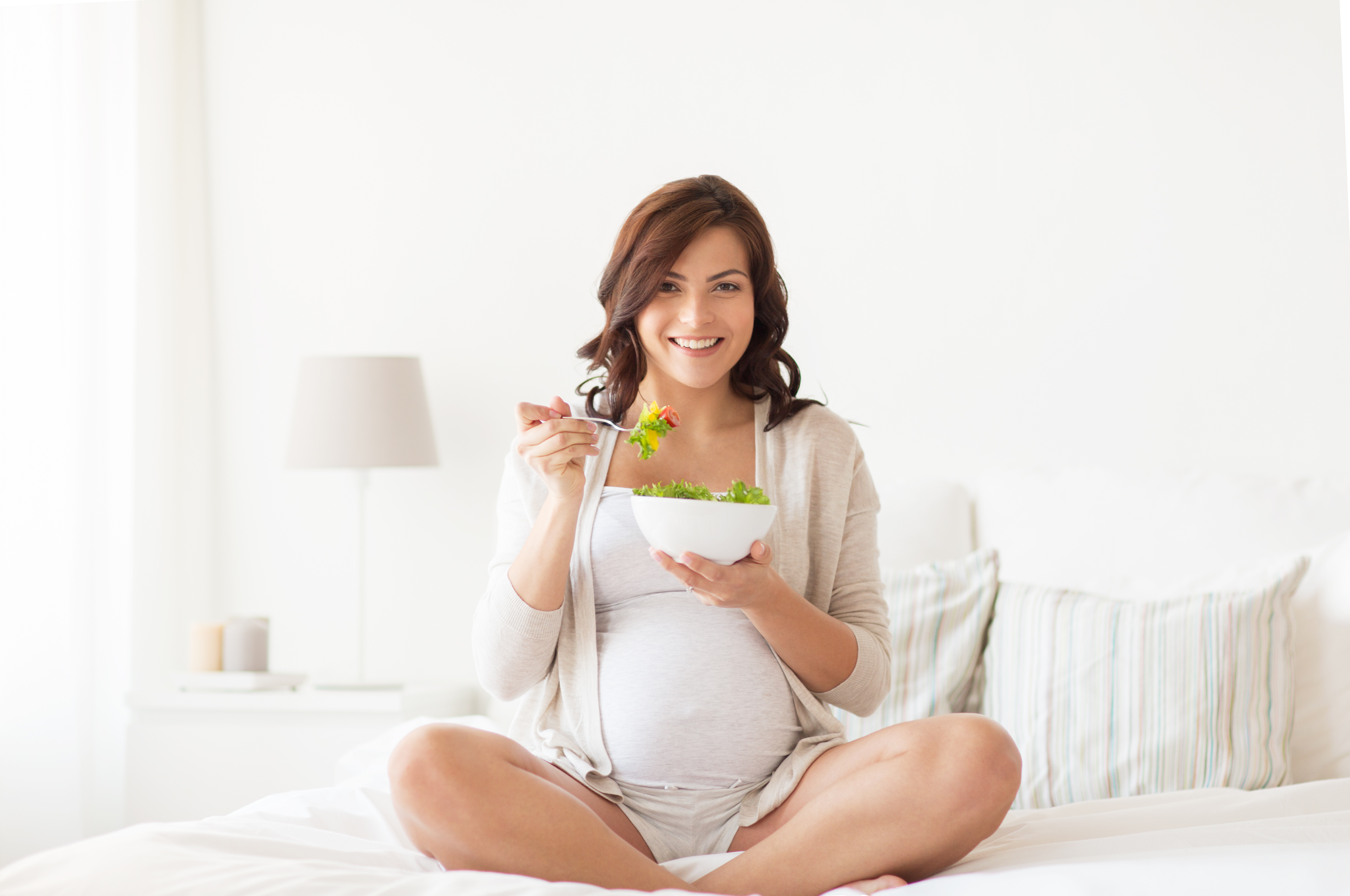 happy pregnant woman eating salad at home
