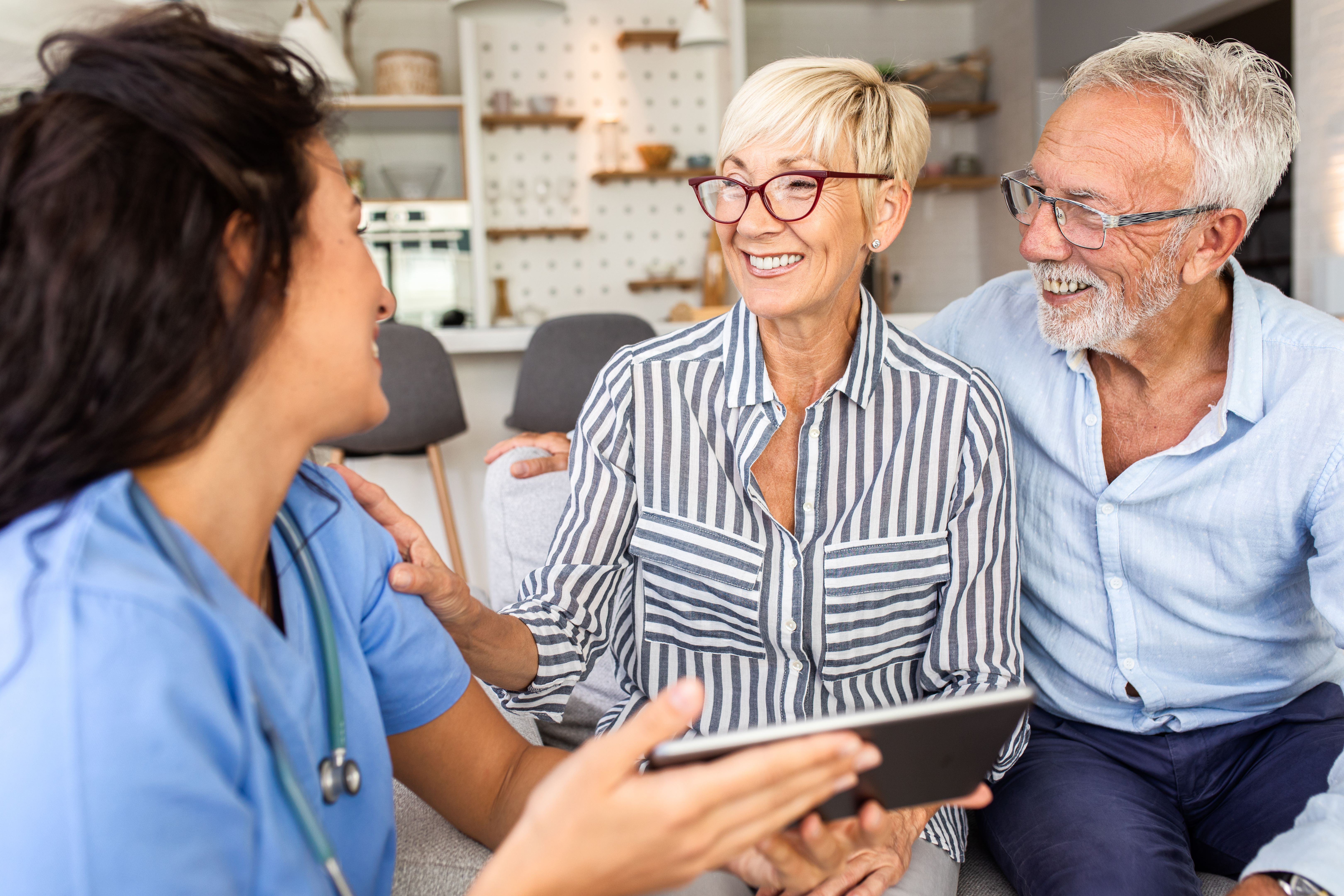 Female nurse talking to seniors patients while being in a home visit.