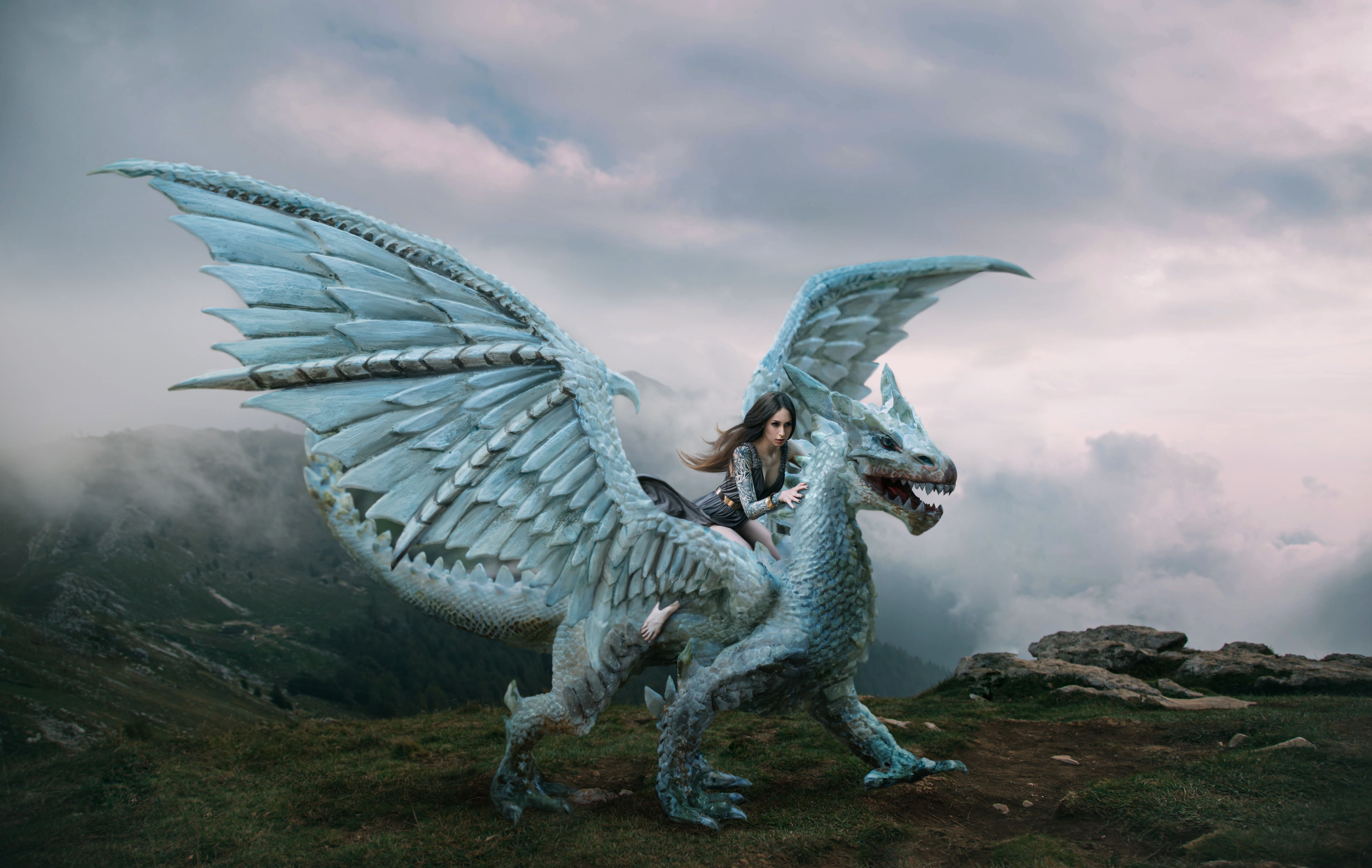A young woman sits astride a dragon. Fantasy photography. A huge creature with spikes and wings stands on top of a mountain. Beautiful nature sky and white clouds. A young woman sits astride a dragon. Fantasy photography. A huge creature with spikes and wings stands on top of a mountain. Beautiful nature sky and white clouds.