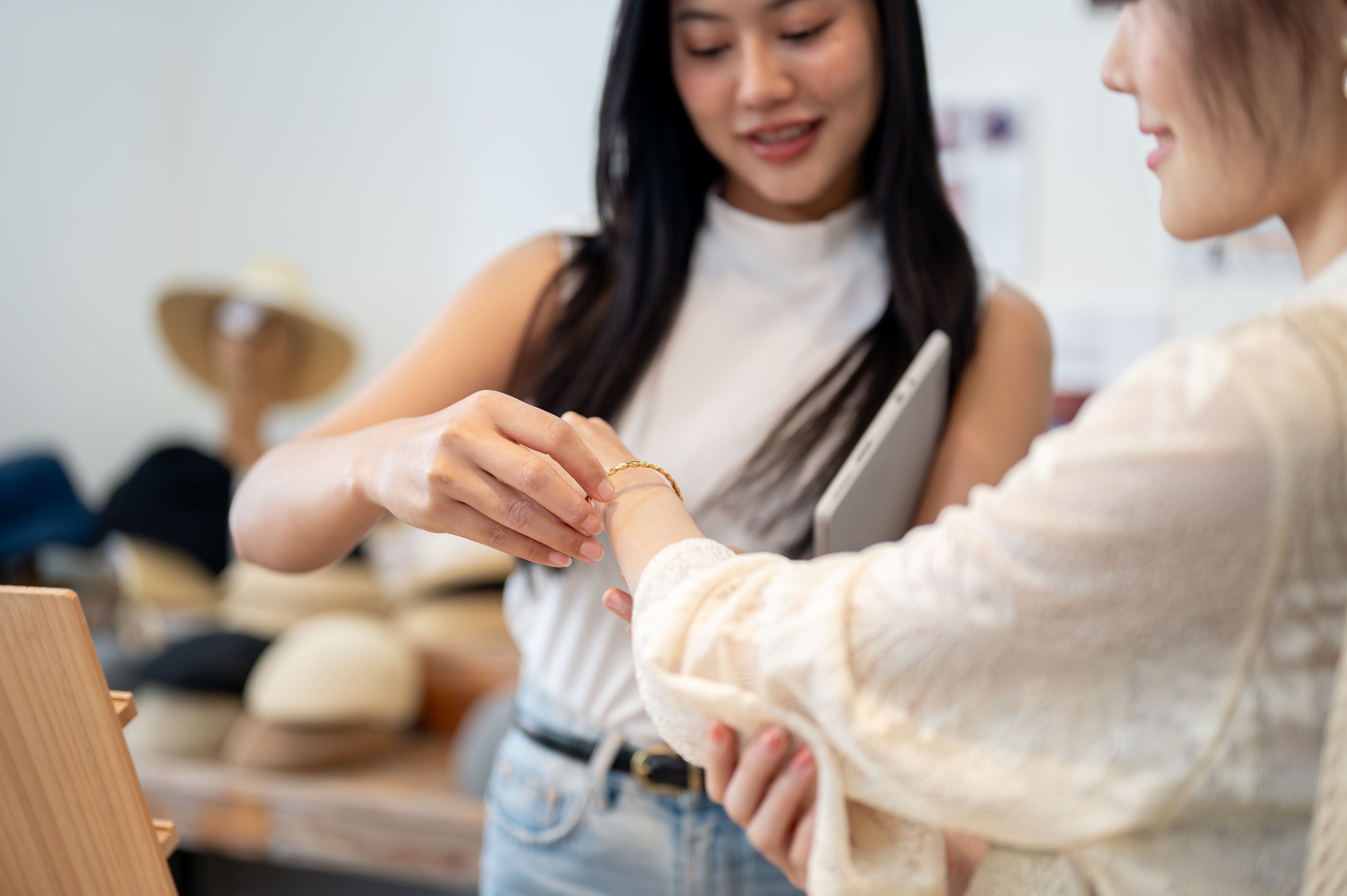 A close-up of a friendly Asian female shop employee is helping a customer try on a bracelet.