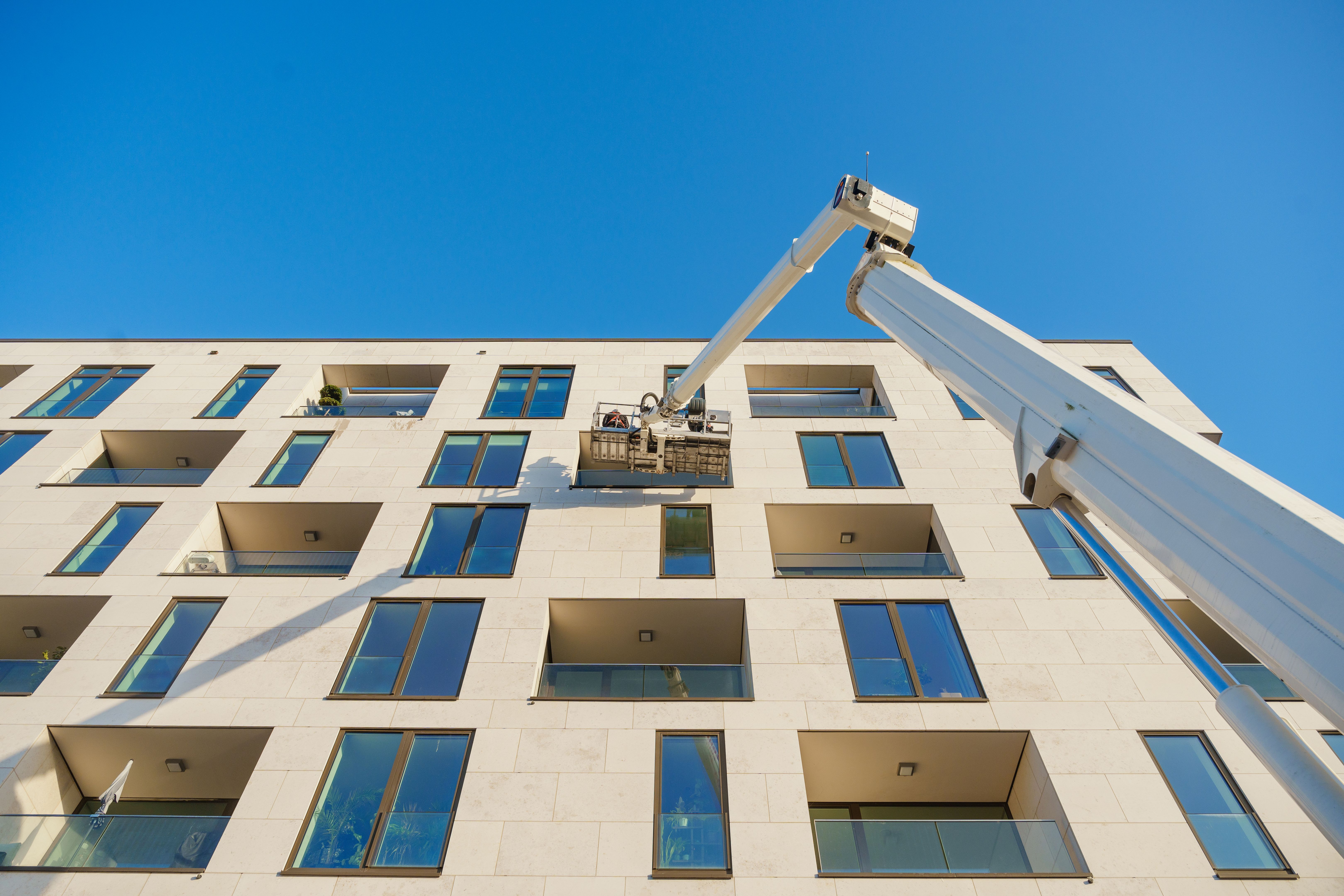 Cleaner worker using a cherry picker to clean a glas facade of a contemporary residential building