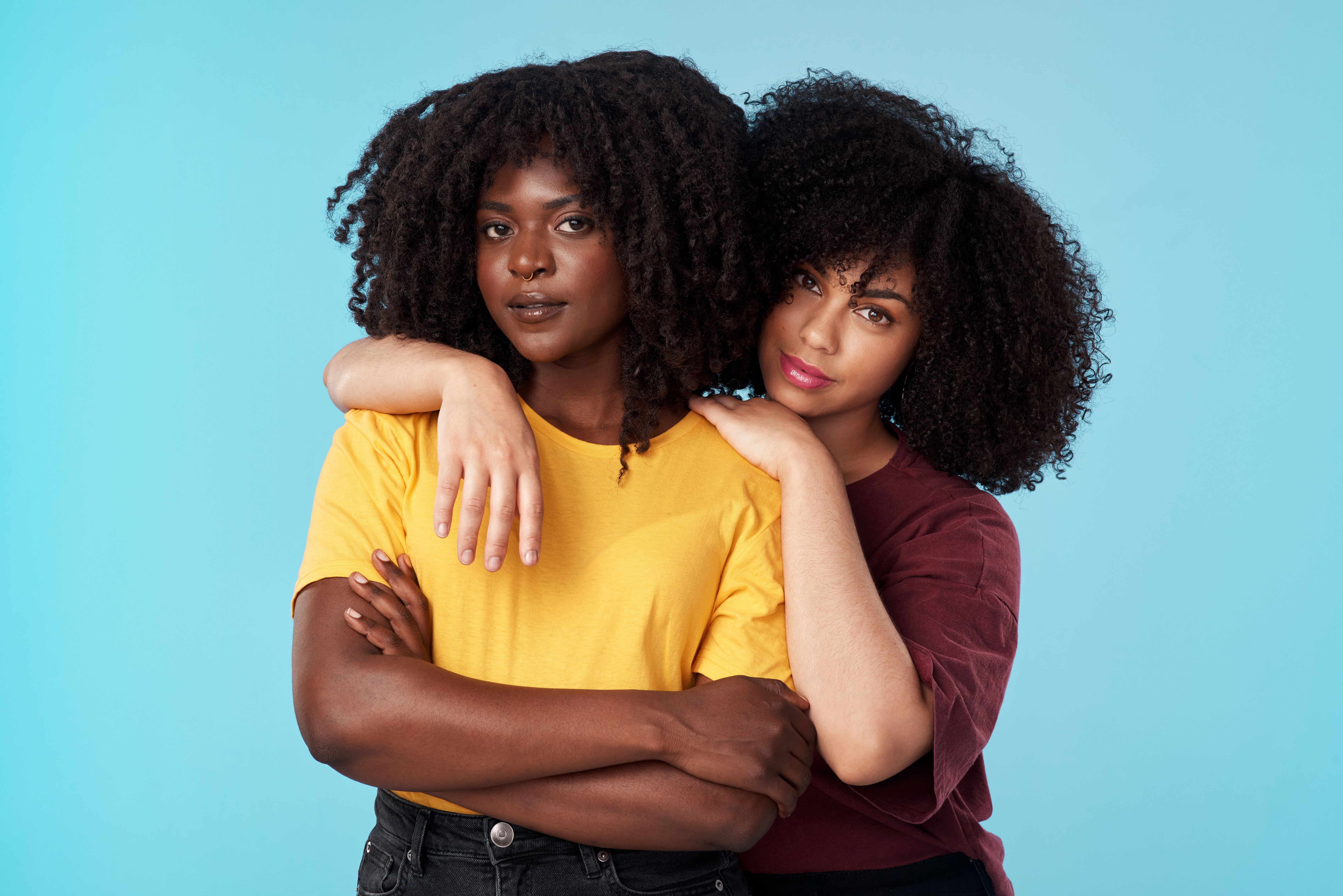 Studio shot of two young women embracing each other against a blue background