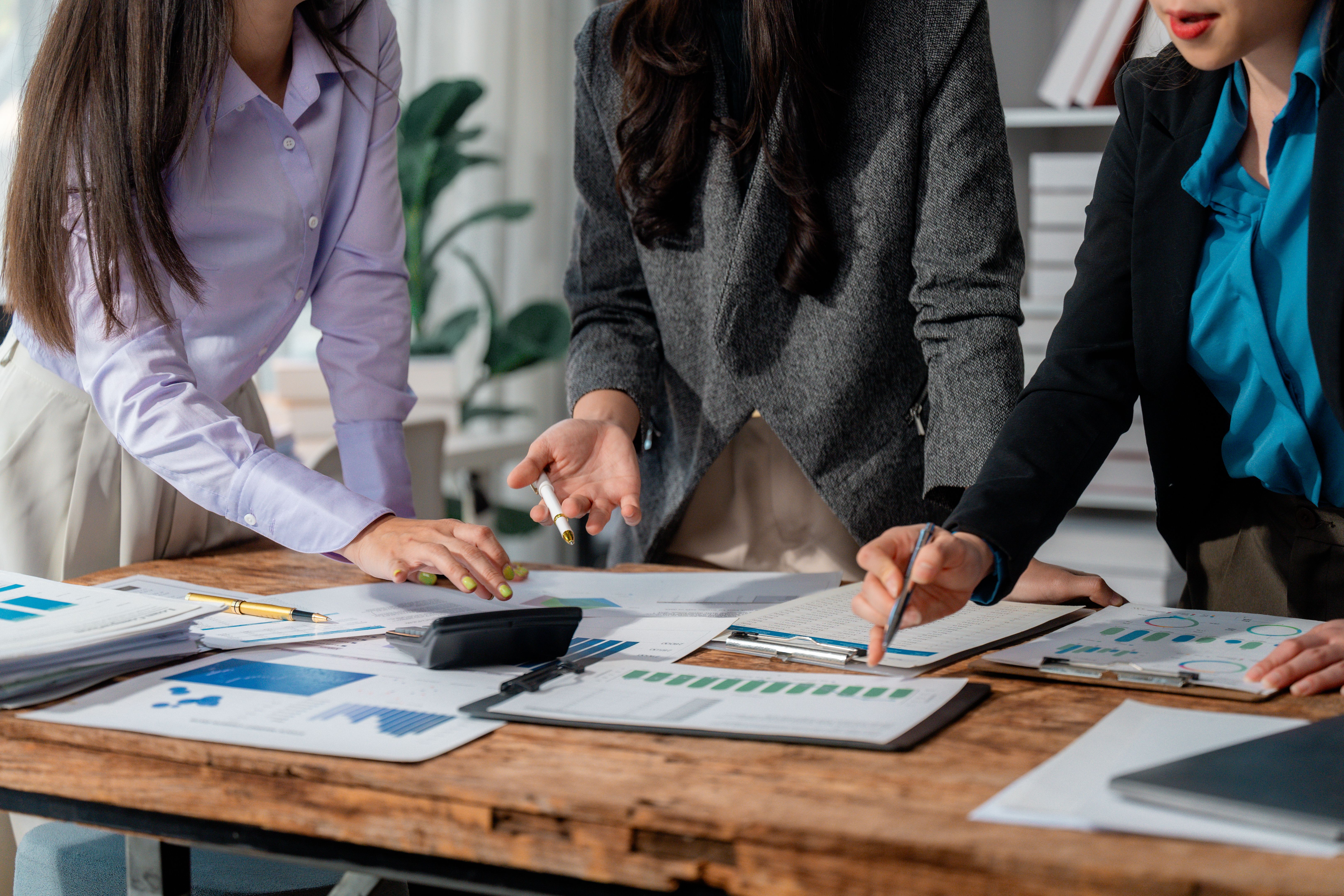 Professional businesswomen reviewing financial documents, analyzing market data, strategizing company growth while working closely in modern office setting