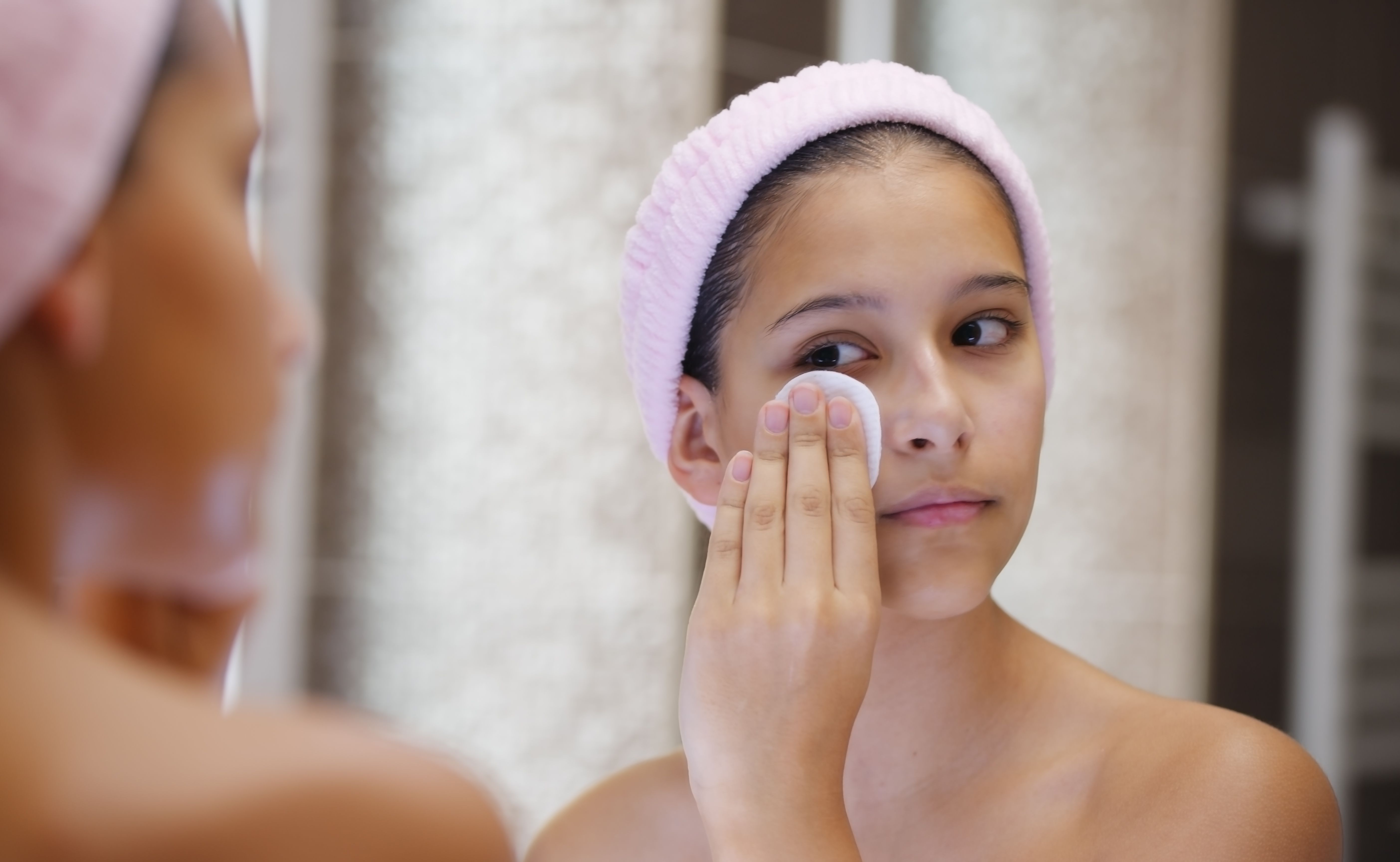 Teenage girl is wiping her face with a cotton pad; removing rest cosmetics or make up. Teenage girl is wiping her face with a cotton pad; removing rest cosmetics or make up.