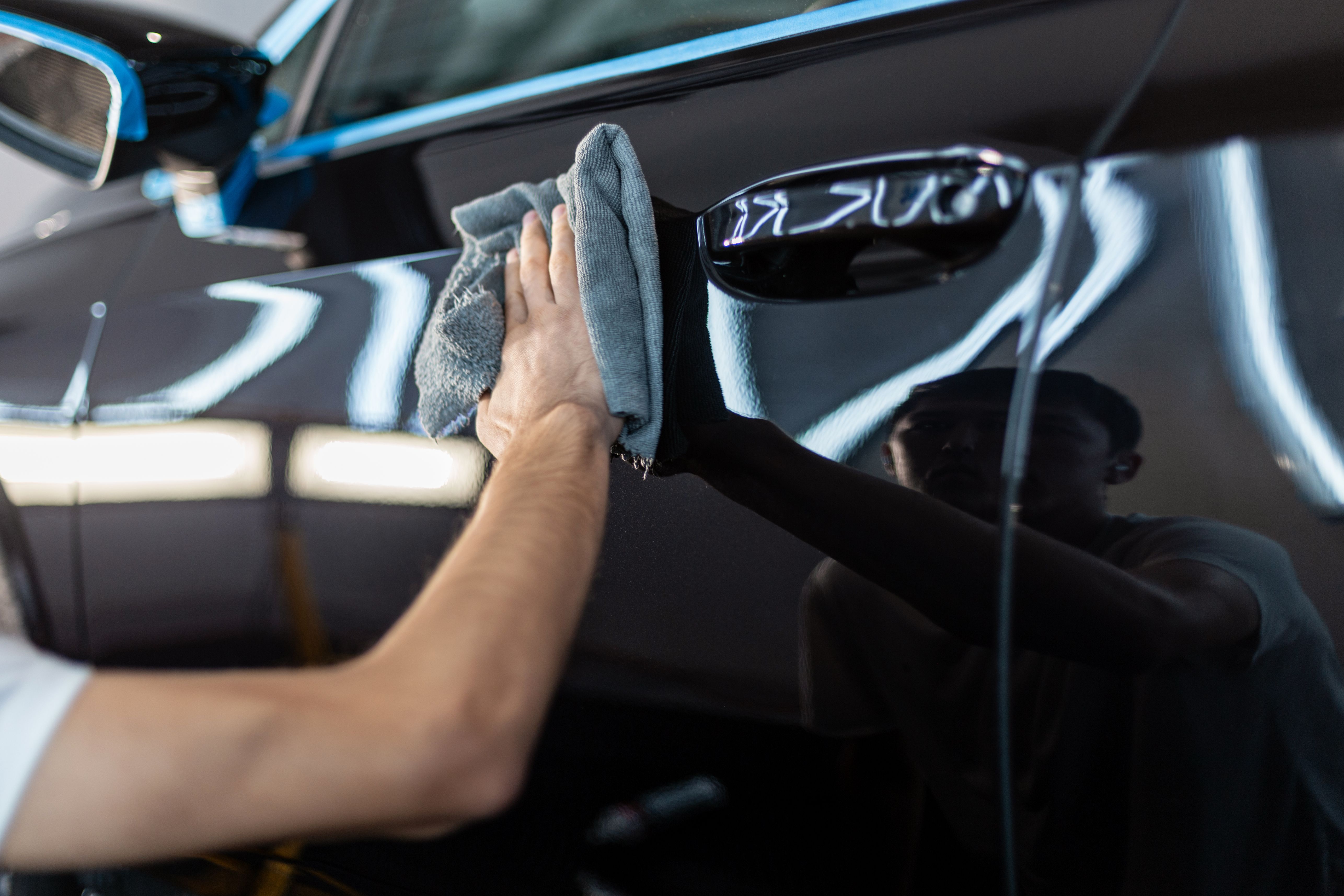Professional man wiping car with cloth after polishing in detailing center. Car varnish care