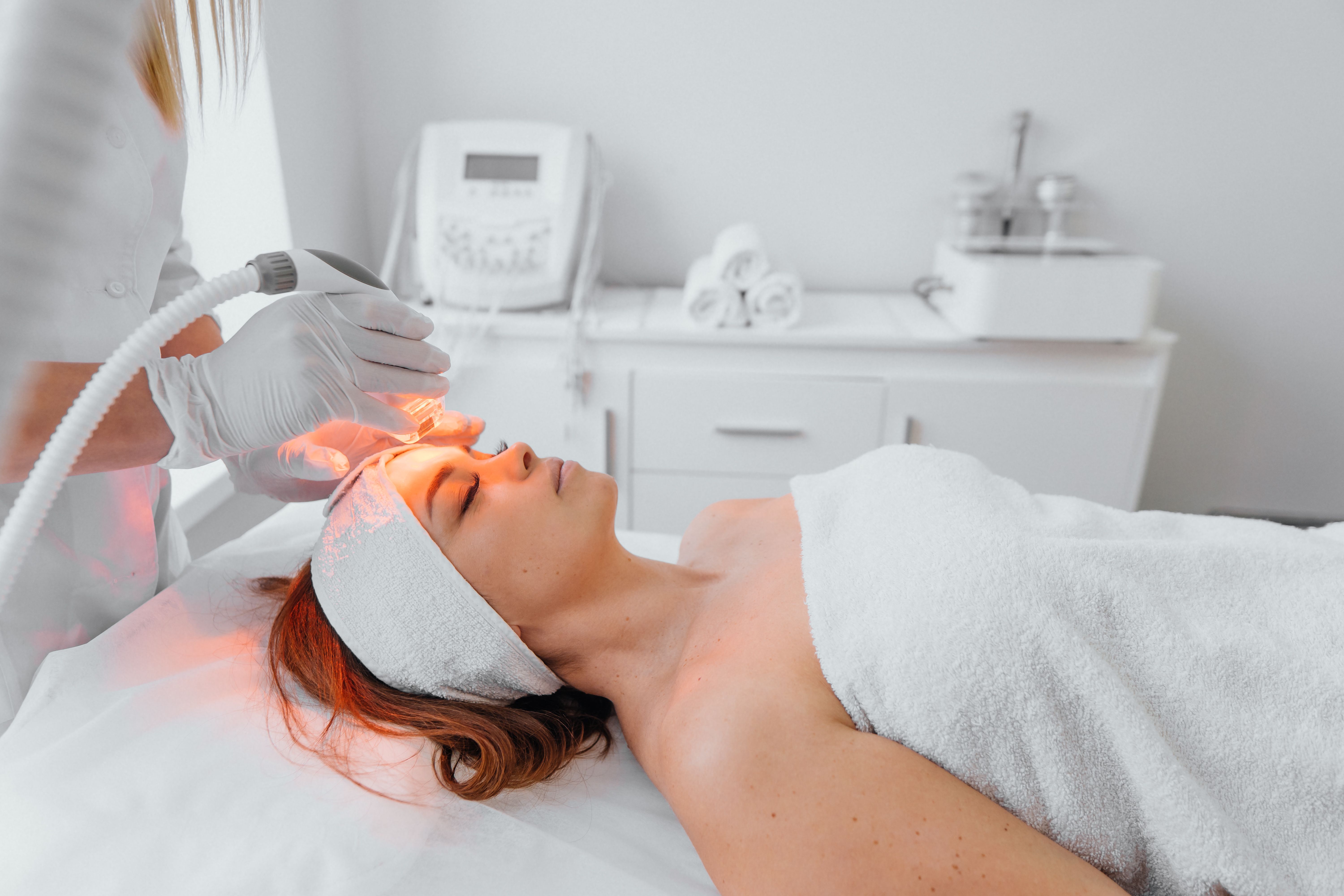 Radiofrequency face lifting. The beautician performs the procedure in the beauty salon using an LED device. Hardware anti-aging procedure. Young woman lying resting and relaxing