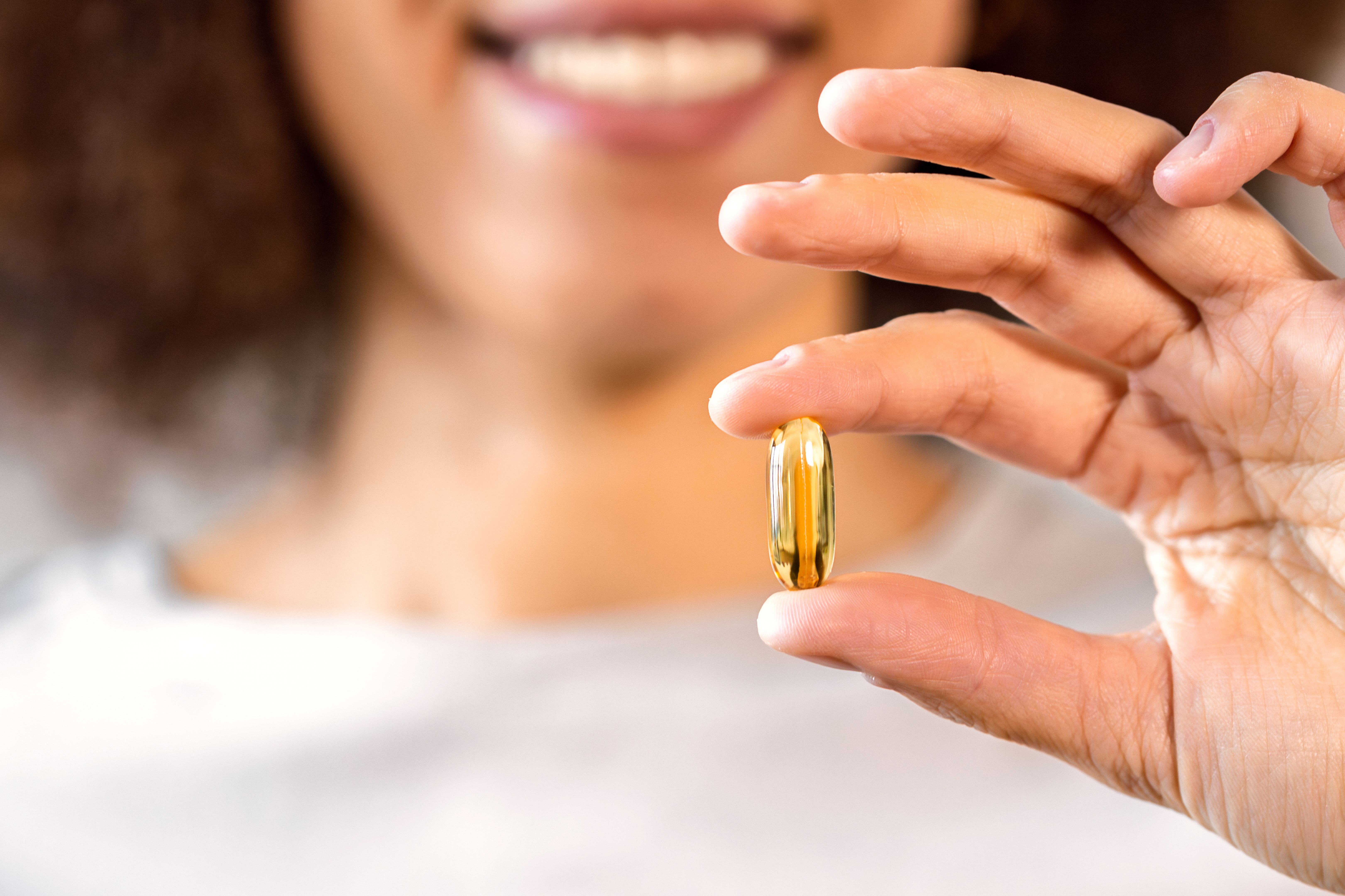 Woman holding golden omega 3 capsule with smile Woman holding golden omega 3 capsule with smile