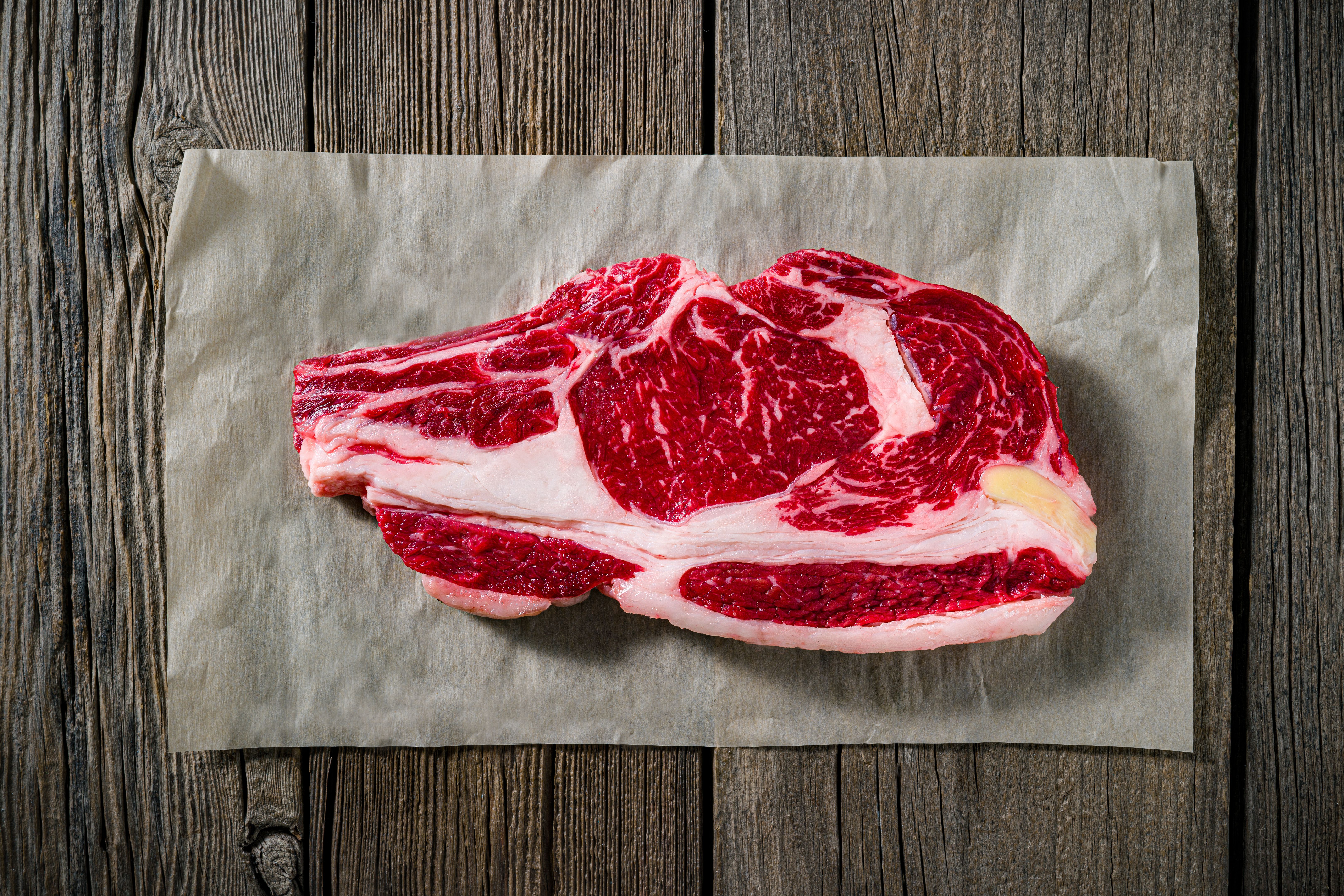 Beef rib steak raw on a butcher paper at supermarket on a rustic dark wood