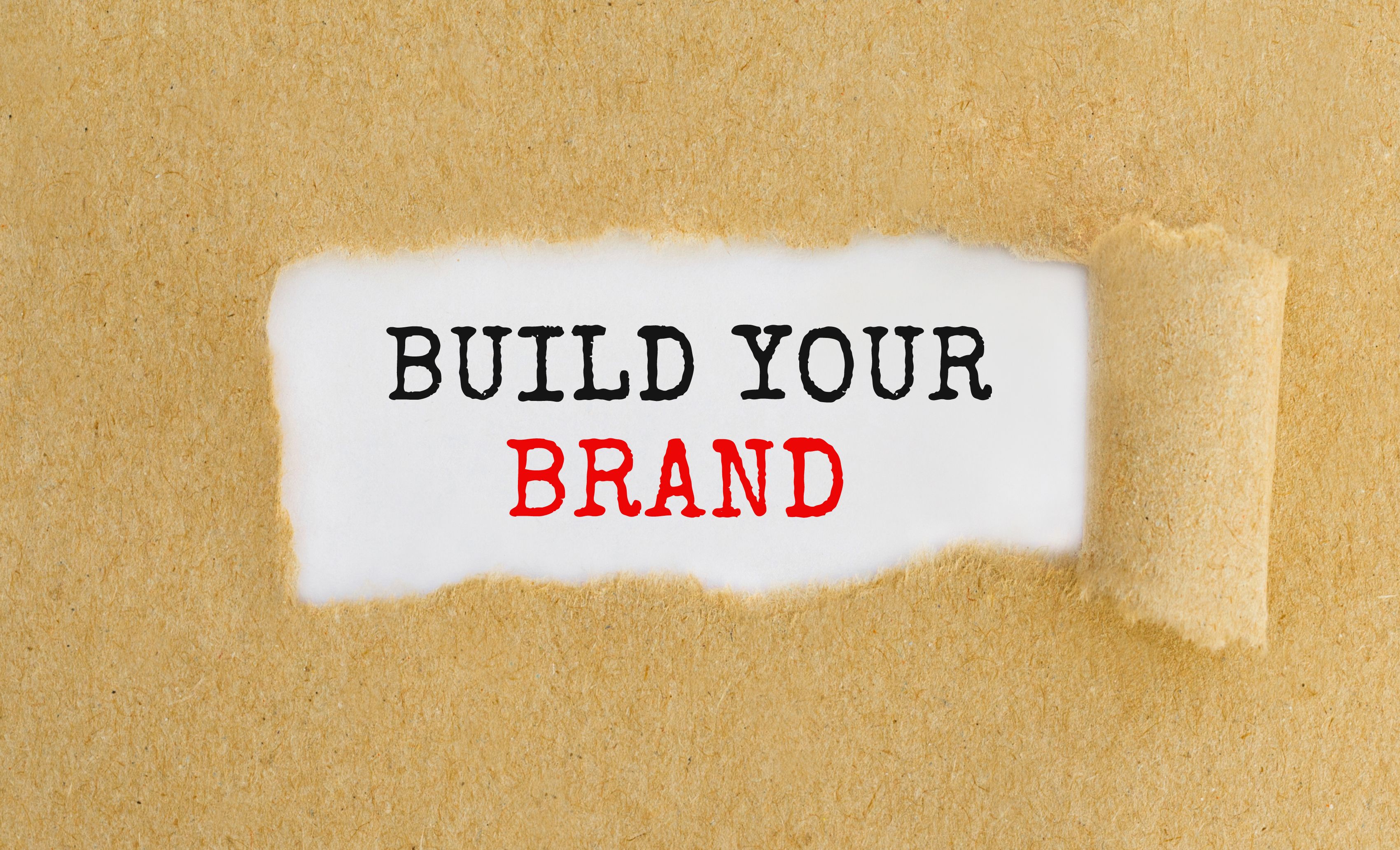 Text Build Your Brand appearing behind ripped brown paper. Text Build Your Brand appearing behind ripped brown paper.