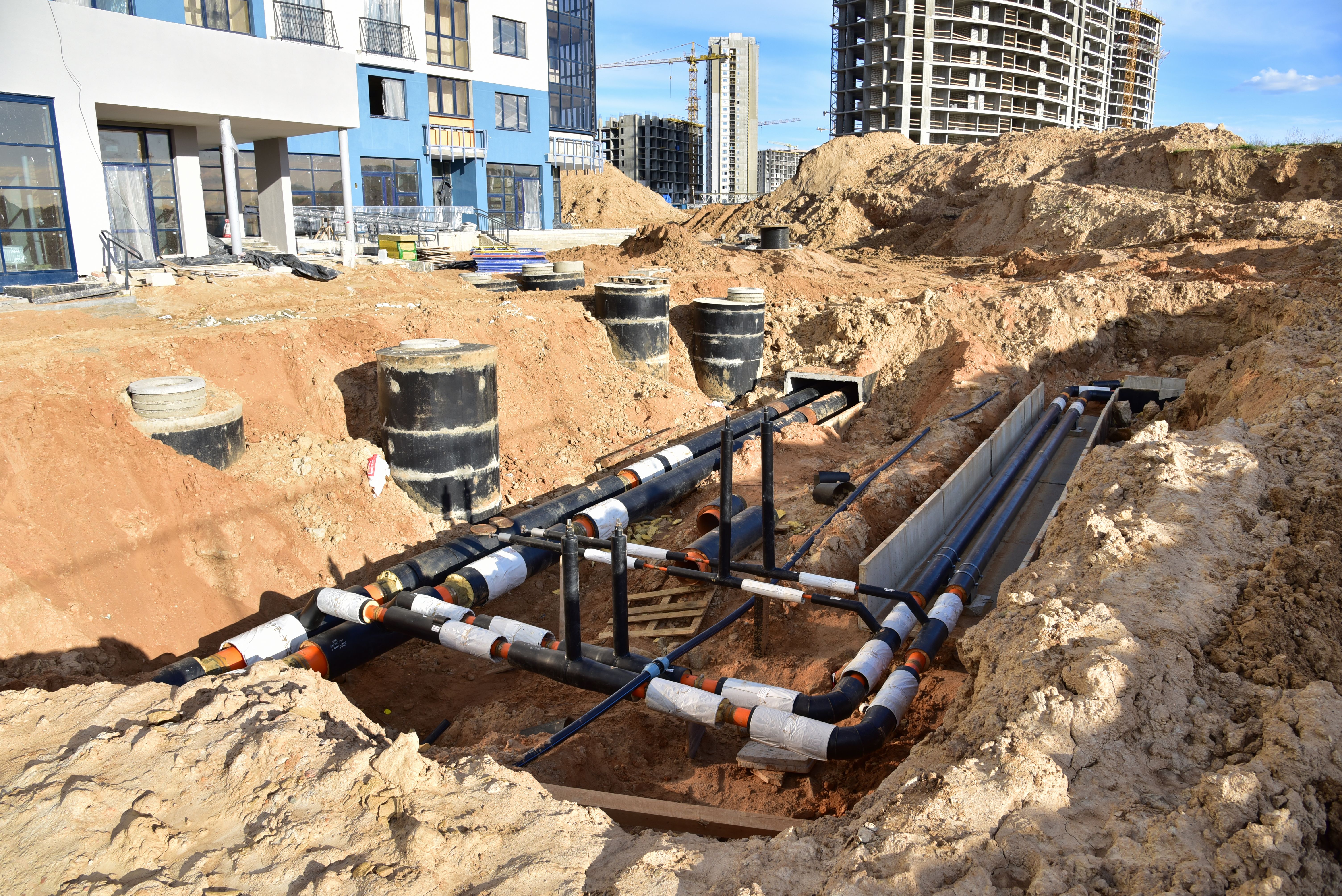 Laying heating pipes in trench at construction site. Installing concrete sewer wells and underground storm systems of sanitary water main.