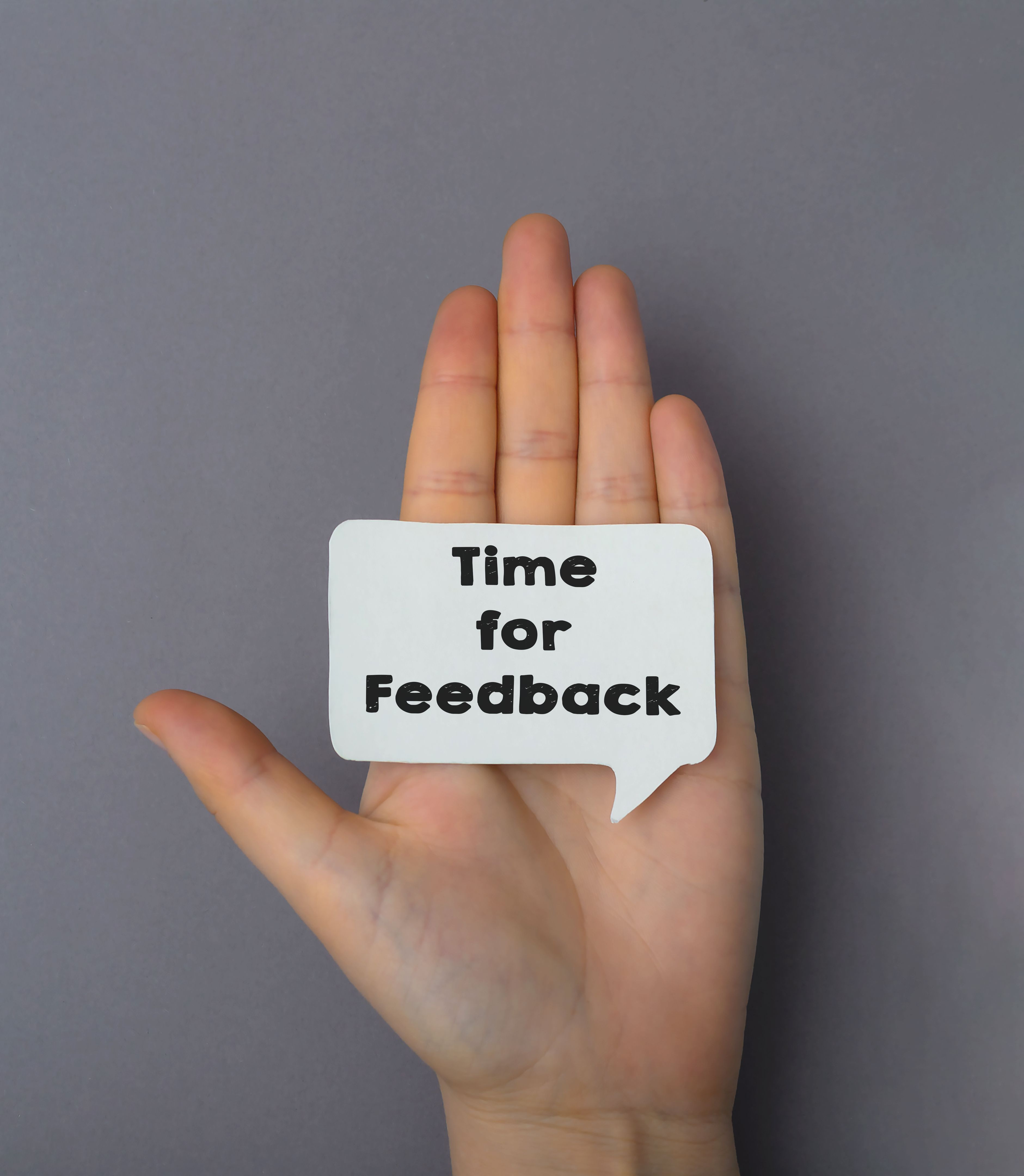 text on white business card time for feedback. Female hand on a gray background with a template for design. Business and advertising concept text on white business card time for feedback. Female hand on a gray background with a template for design. Business and advertising concept