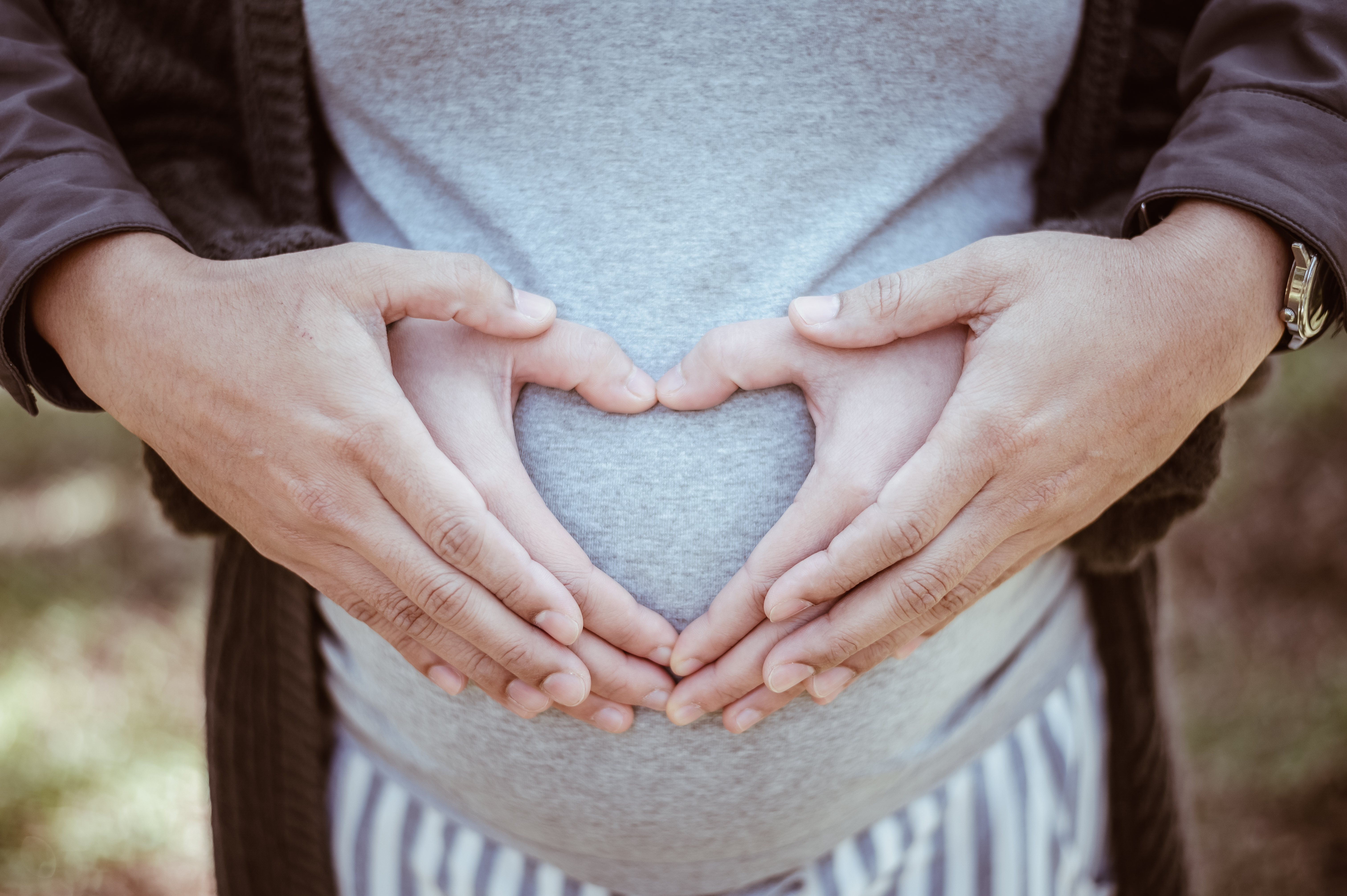 Cropped image of lovely couple do hand sign a heart shape and hugging the tummy. Cropped image of lovely couple do hand sign a heart shape and hugging the tummy.