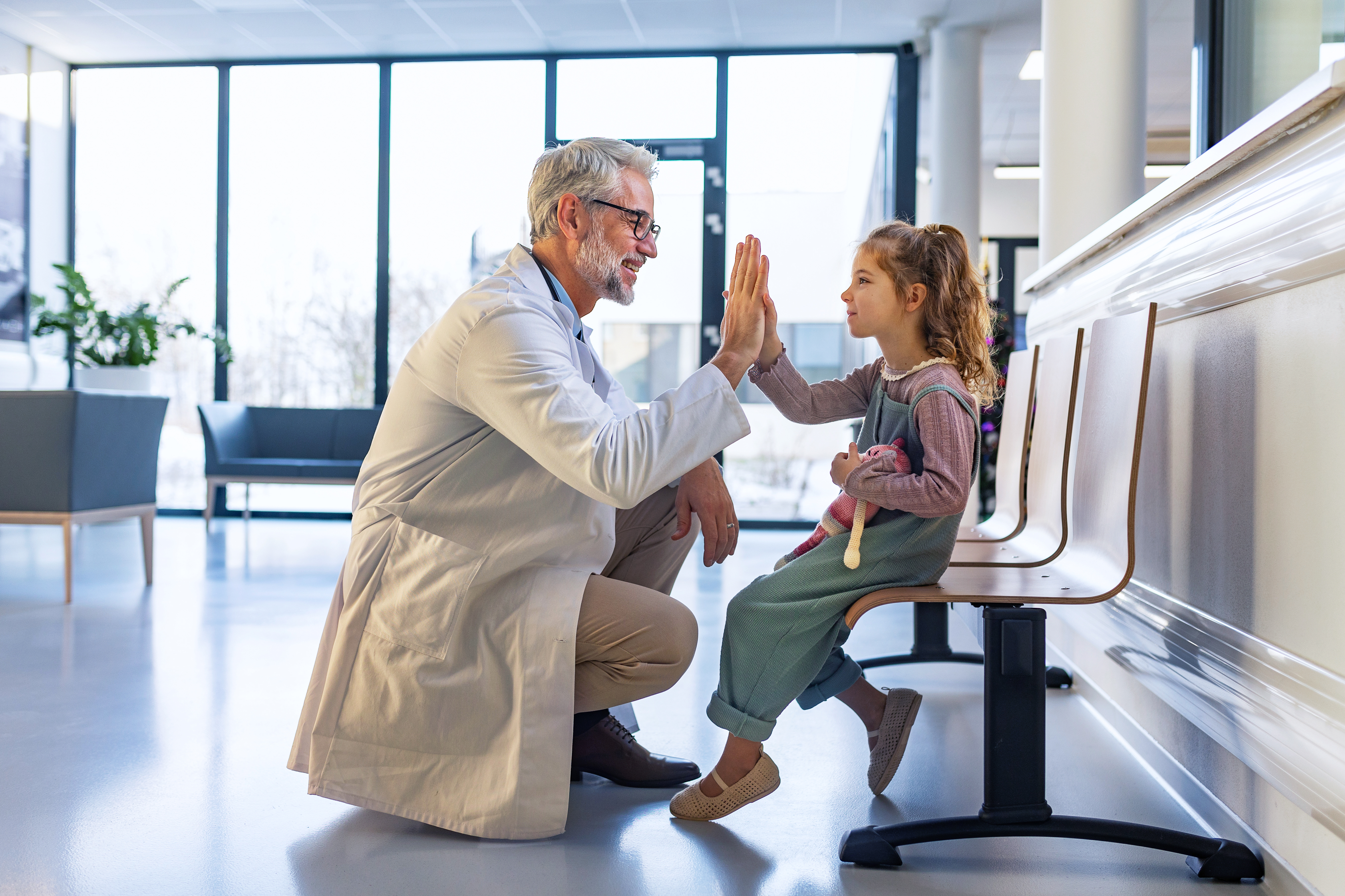 Friendly pediatrician giving high five to little patient. Cute preschool girl in greeting doctor in hospital corridor.