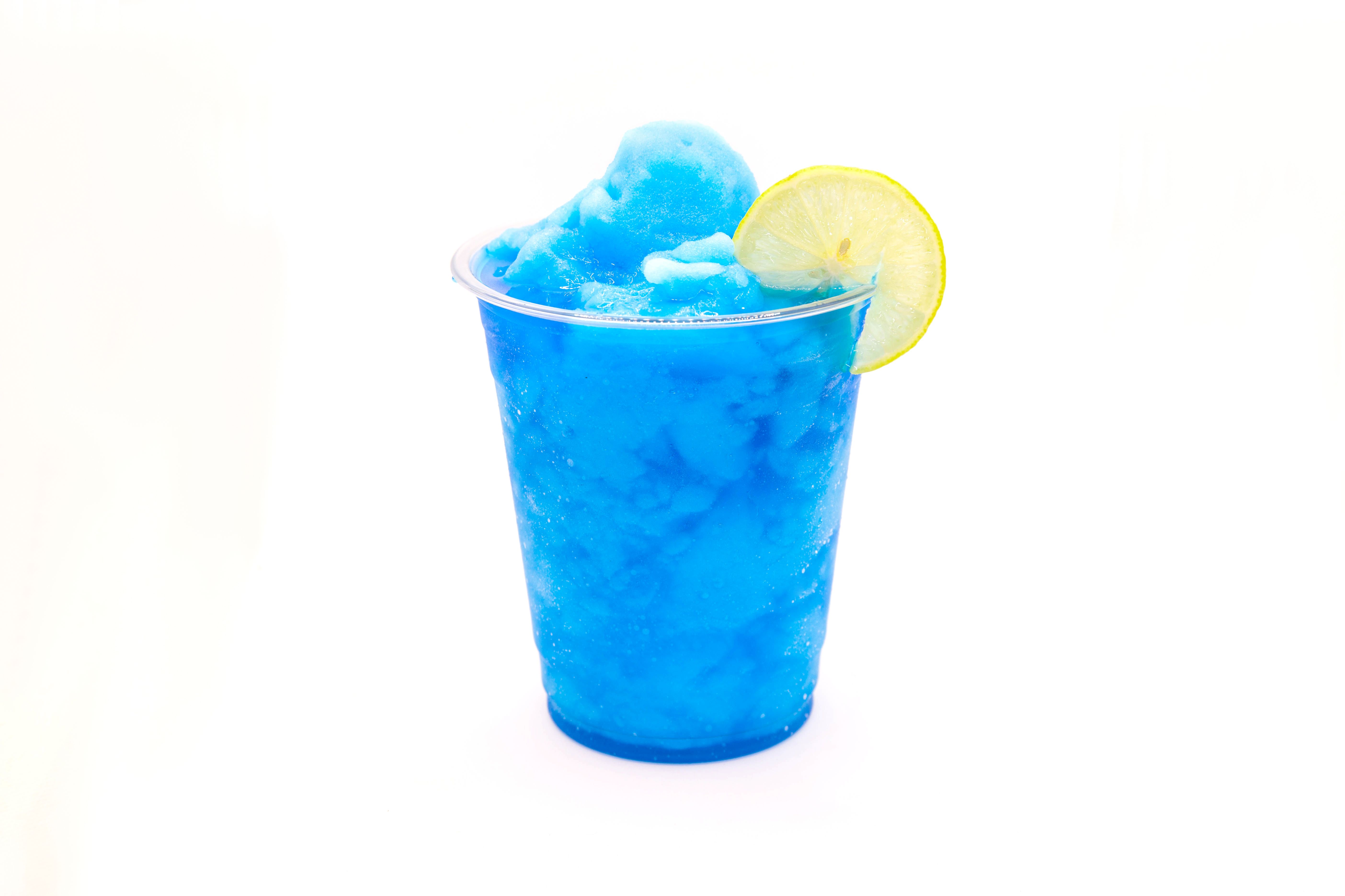 Electric blue lagoon slush lemonade with a slice of lemon in a disposable cup. Electric blue lagoon slush lemonade with a slice of lemon in a disposable cup.