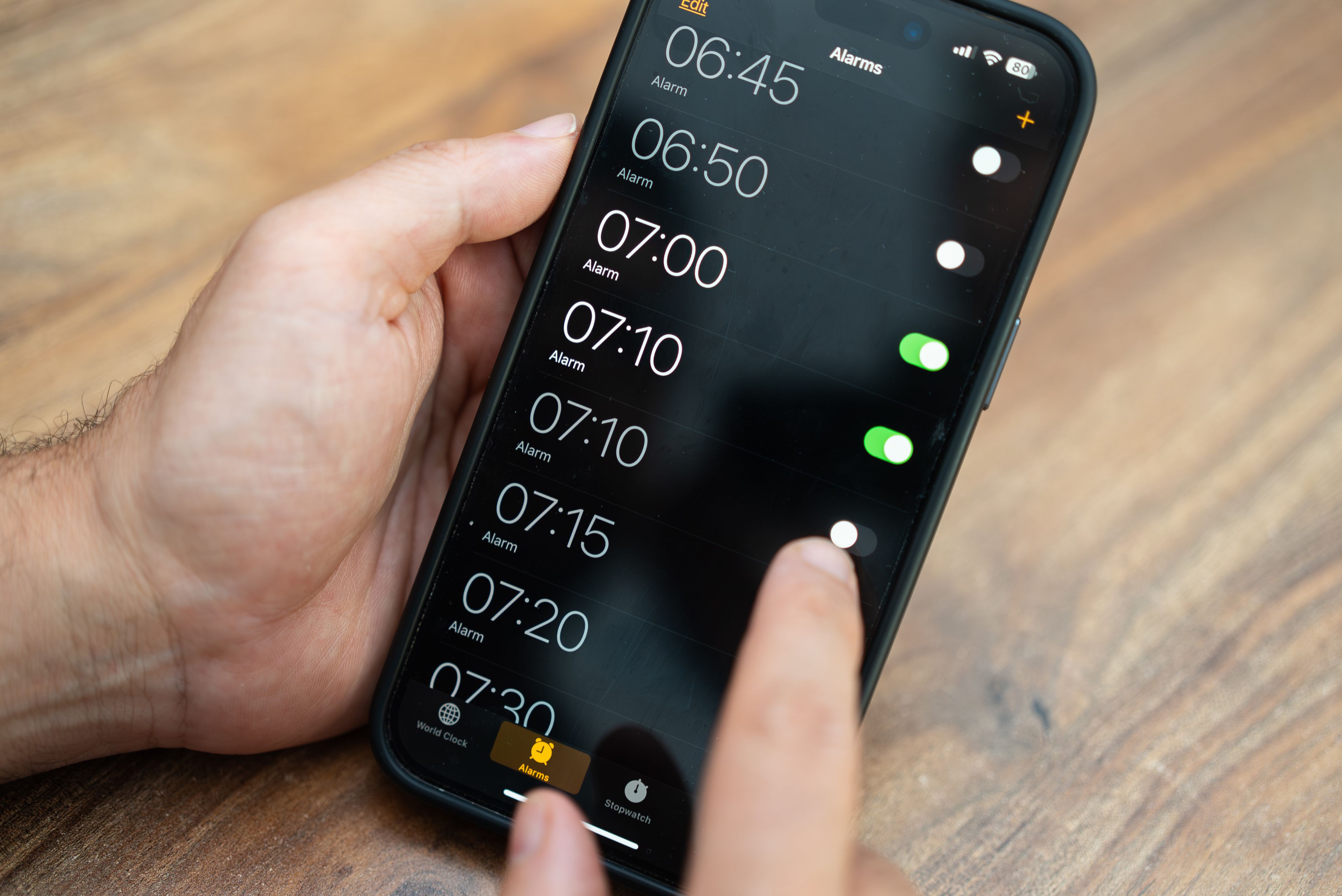 Person setting multiple alarms on a smartphone screen with a wooden background. Time management and wake-up routine concept. Ideal for productivity and daily planning themes.