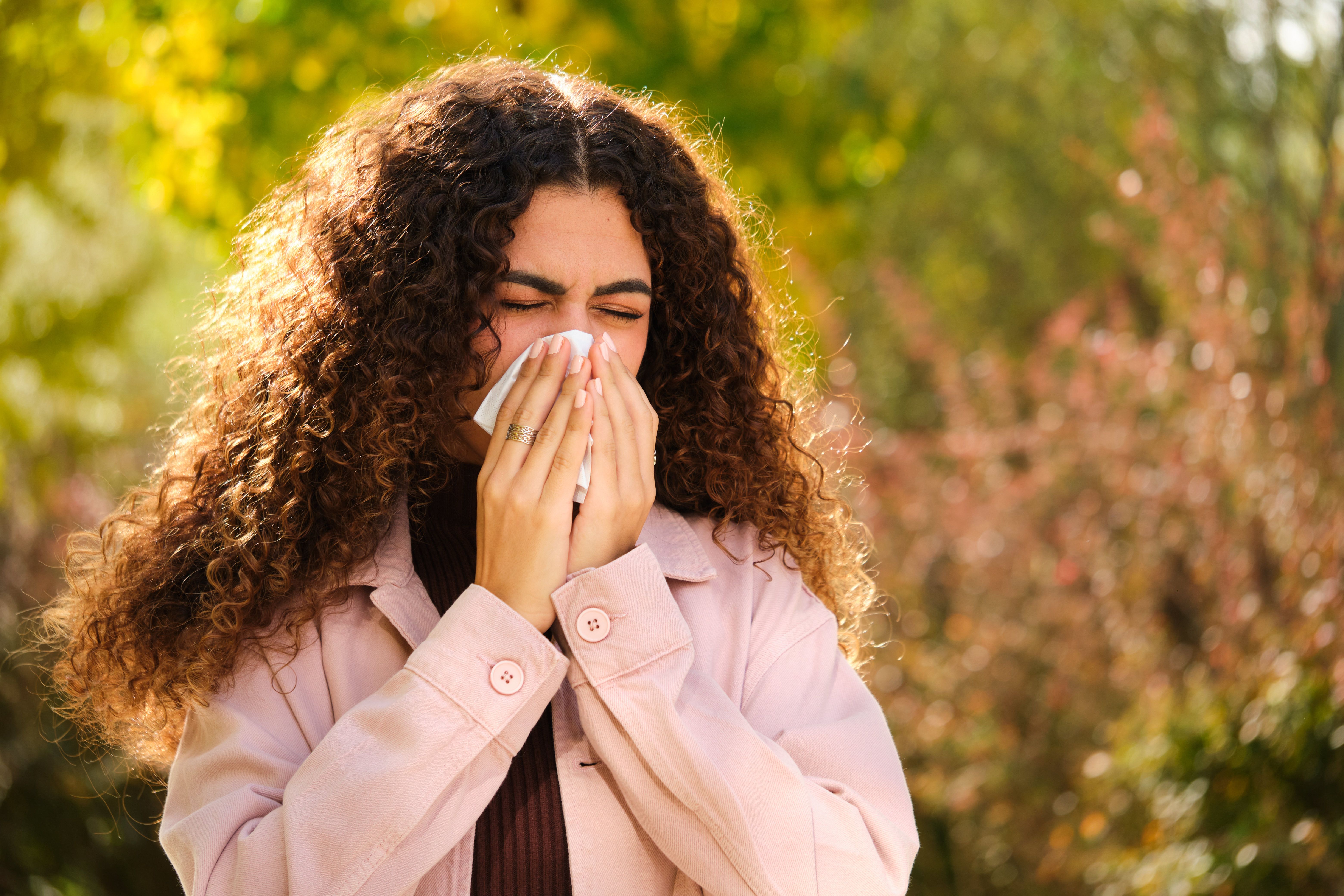 Young Caucasian woman with curly hair blowing your nose in a tissue at street.