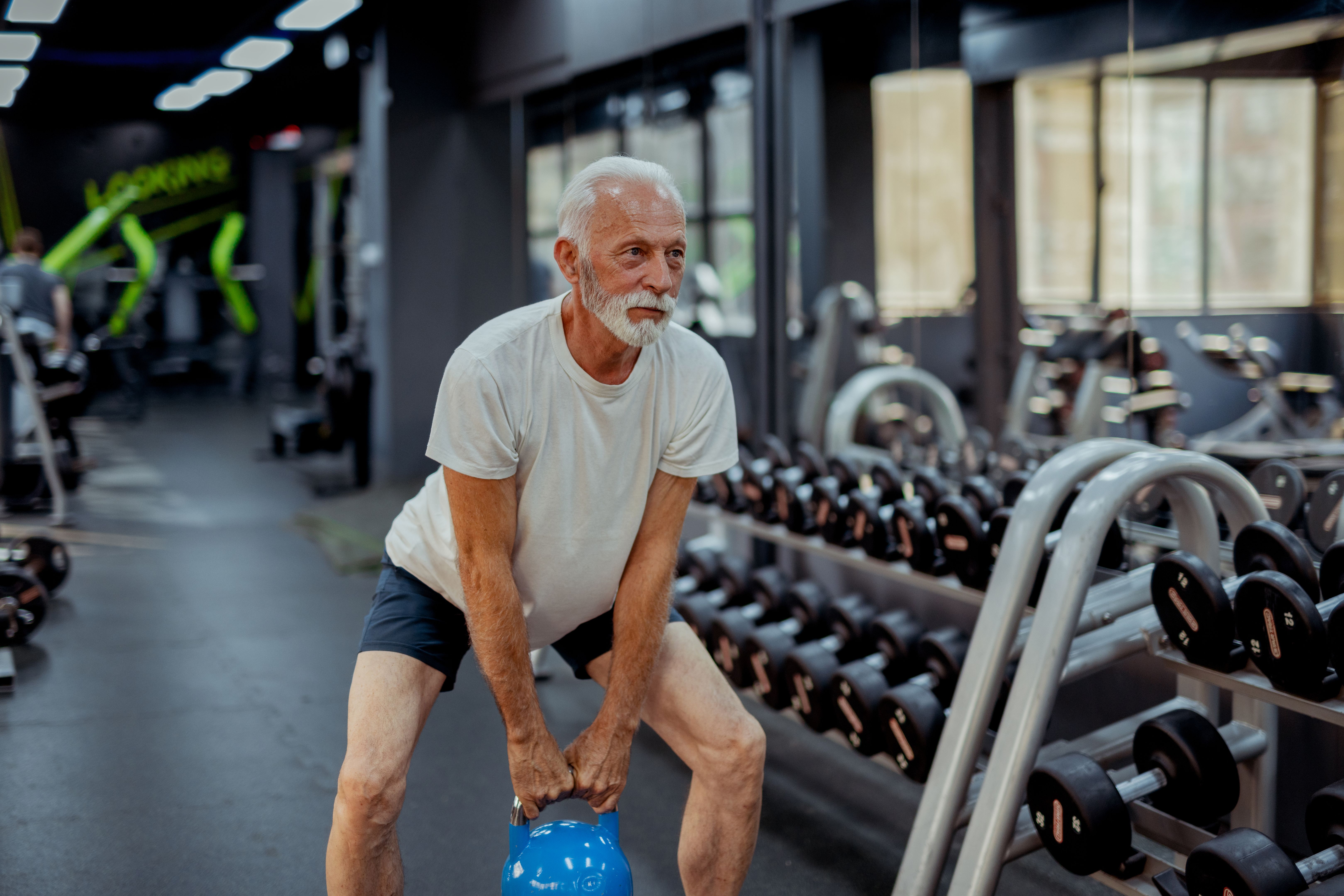 Fit Elderly Man Exercising With Kettlebell in Sport Center
