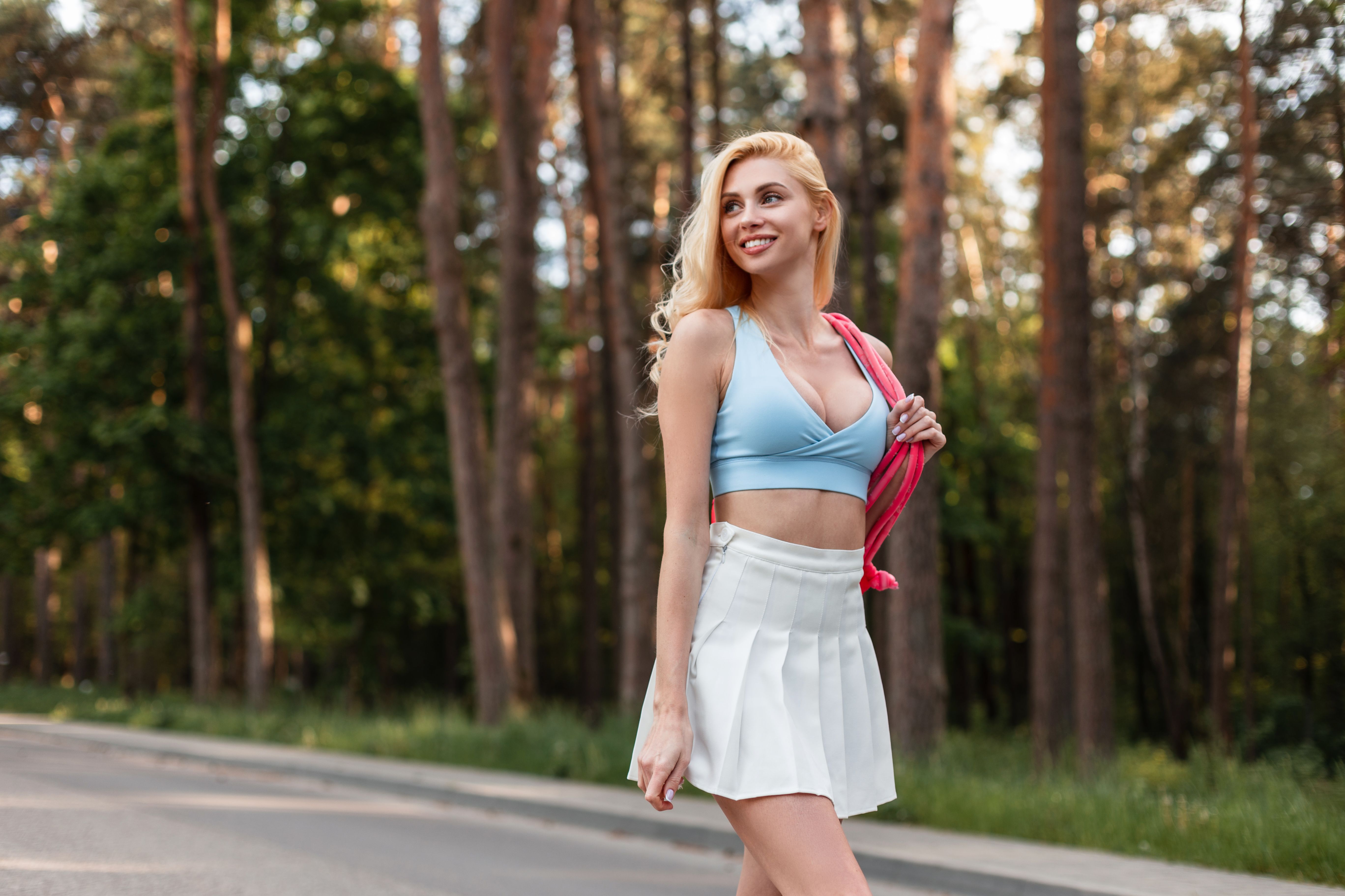 Happy sexy young blonde woman with sweet smile with beautiful body in stylish sportswear with fashion pink backpack travel on forest at sunset. Athletic gorgeous girl model goes play sports in park.