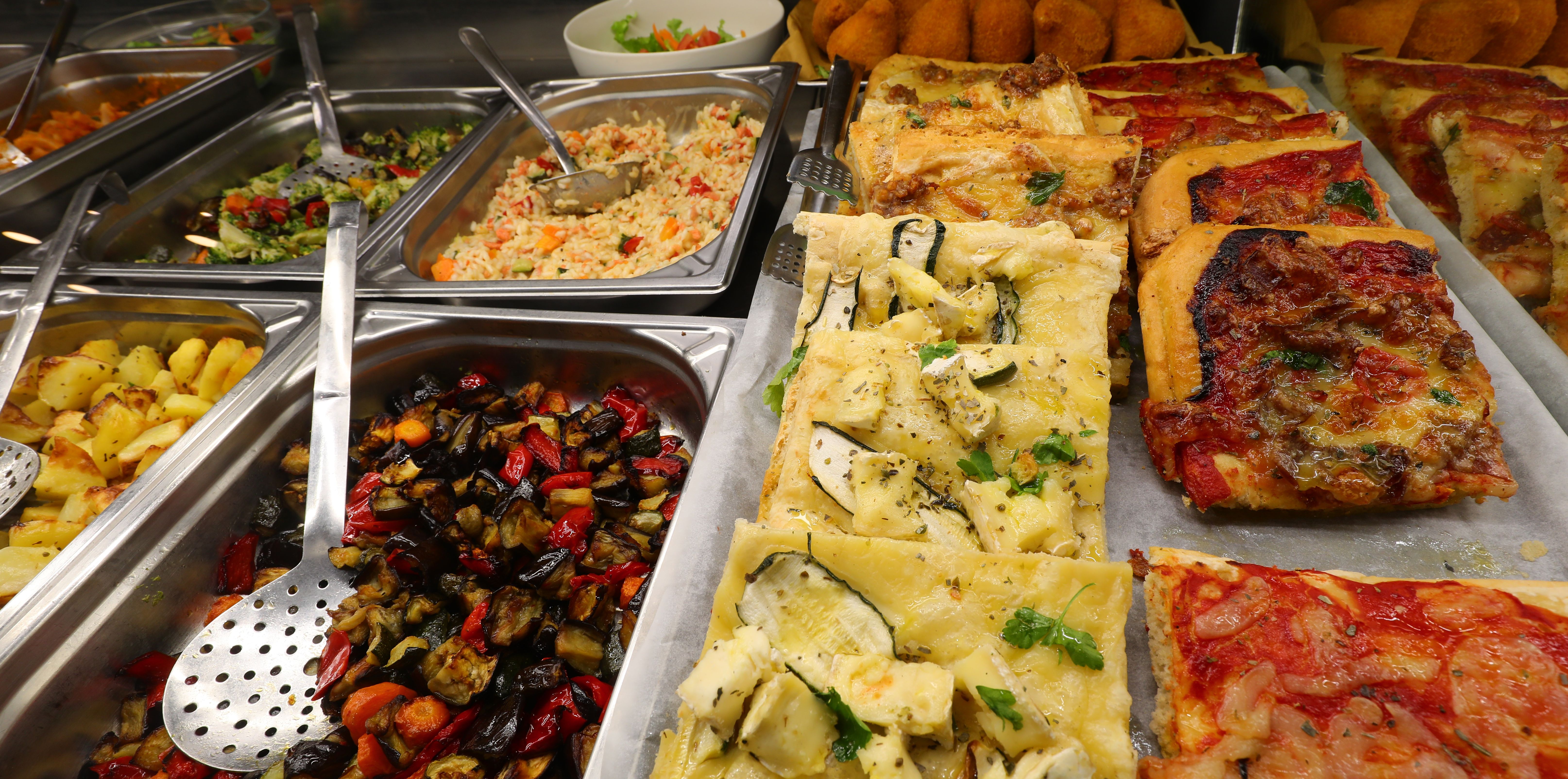 very full trays with hot dishes such as vegetable salad pizza and focaccia in the self-service