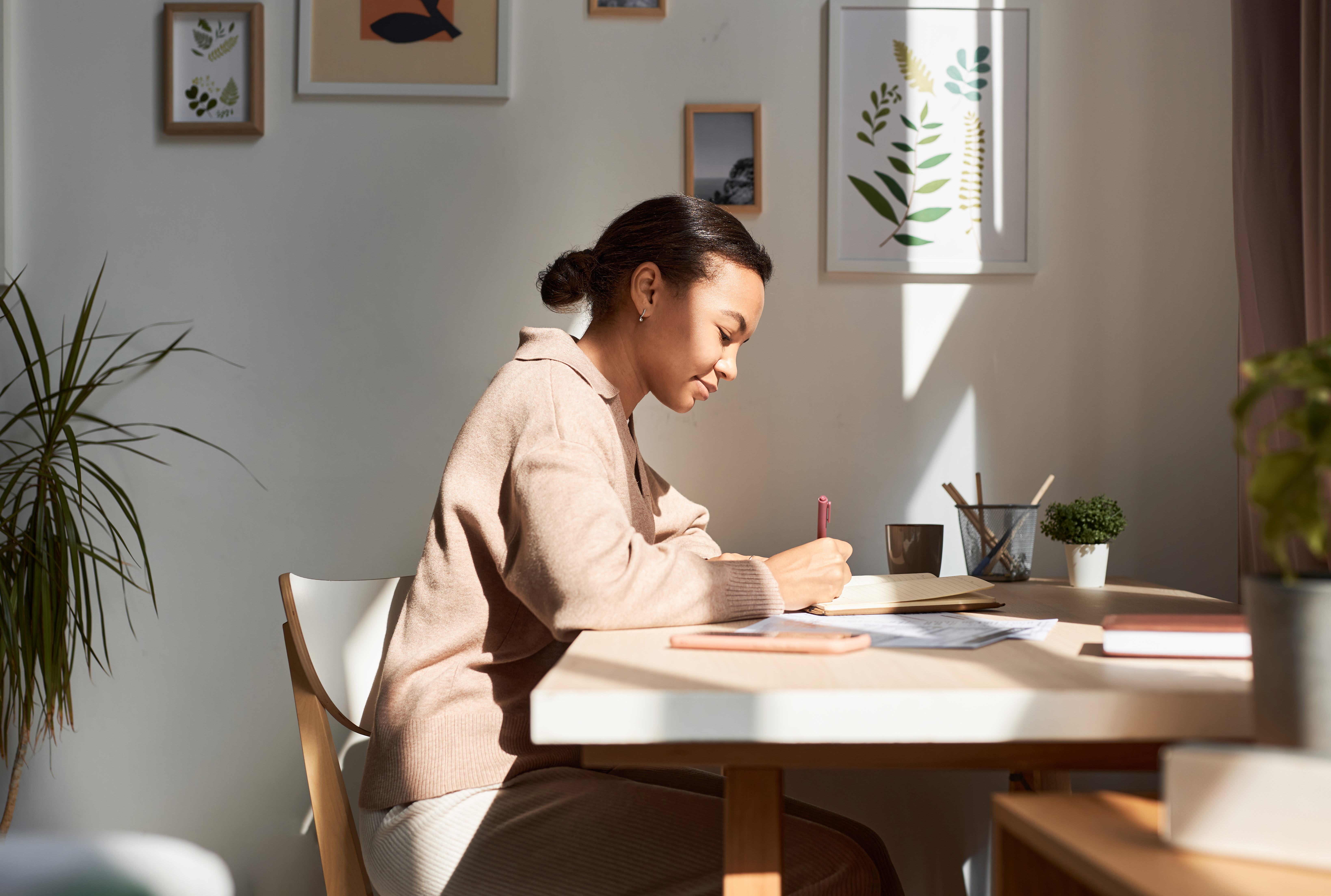 Young African American woman writing in notebook at home with sun rays