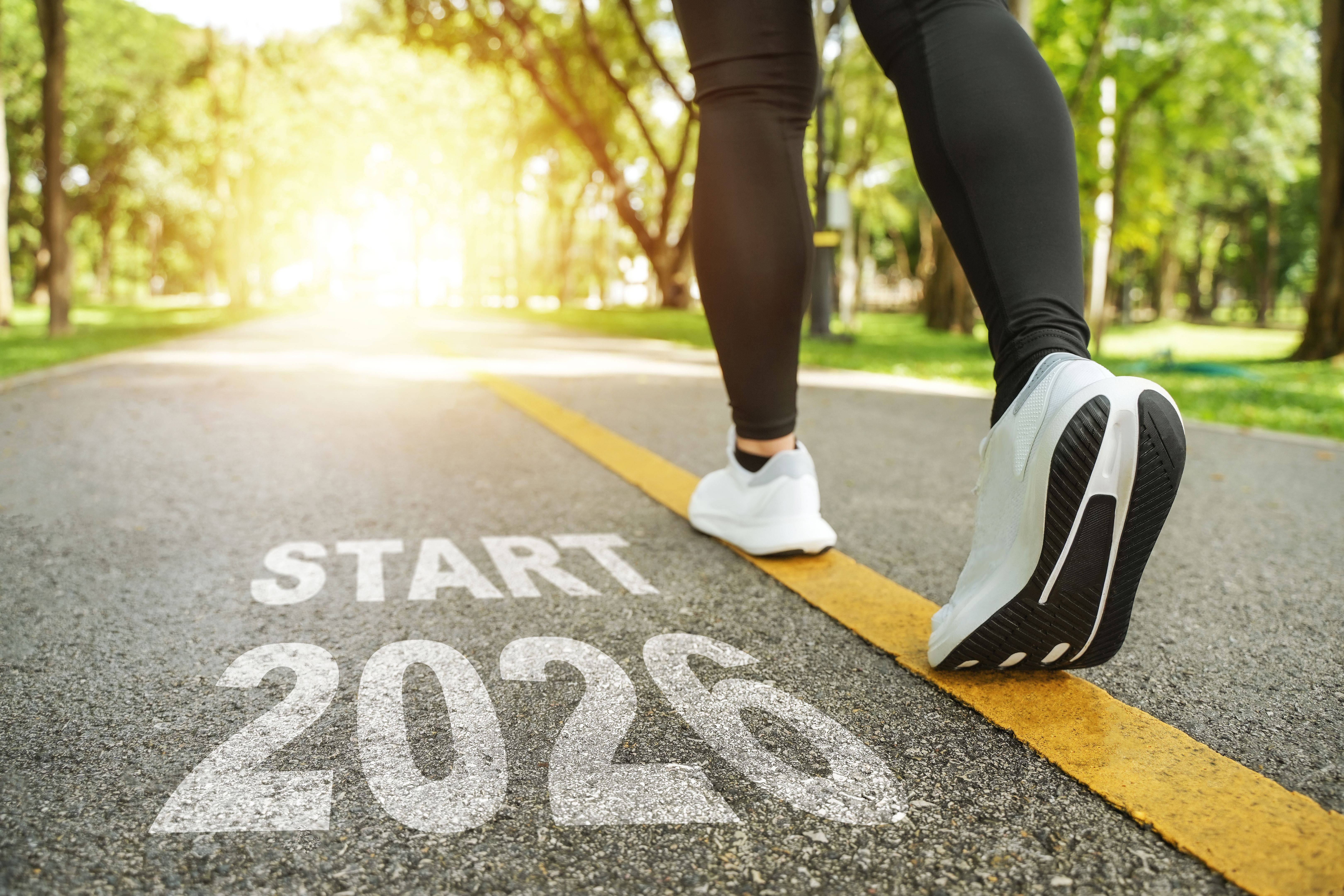New Year 2026 concept. The beginning of success. The text 2026 written on the asphalt road and a female runner is setting off for the new year. Concept of challenges or career paths and changes.