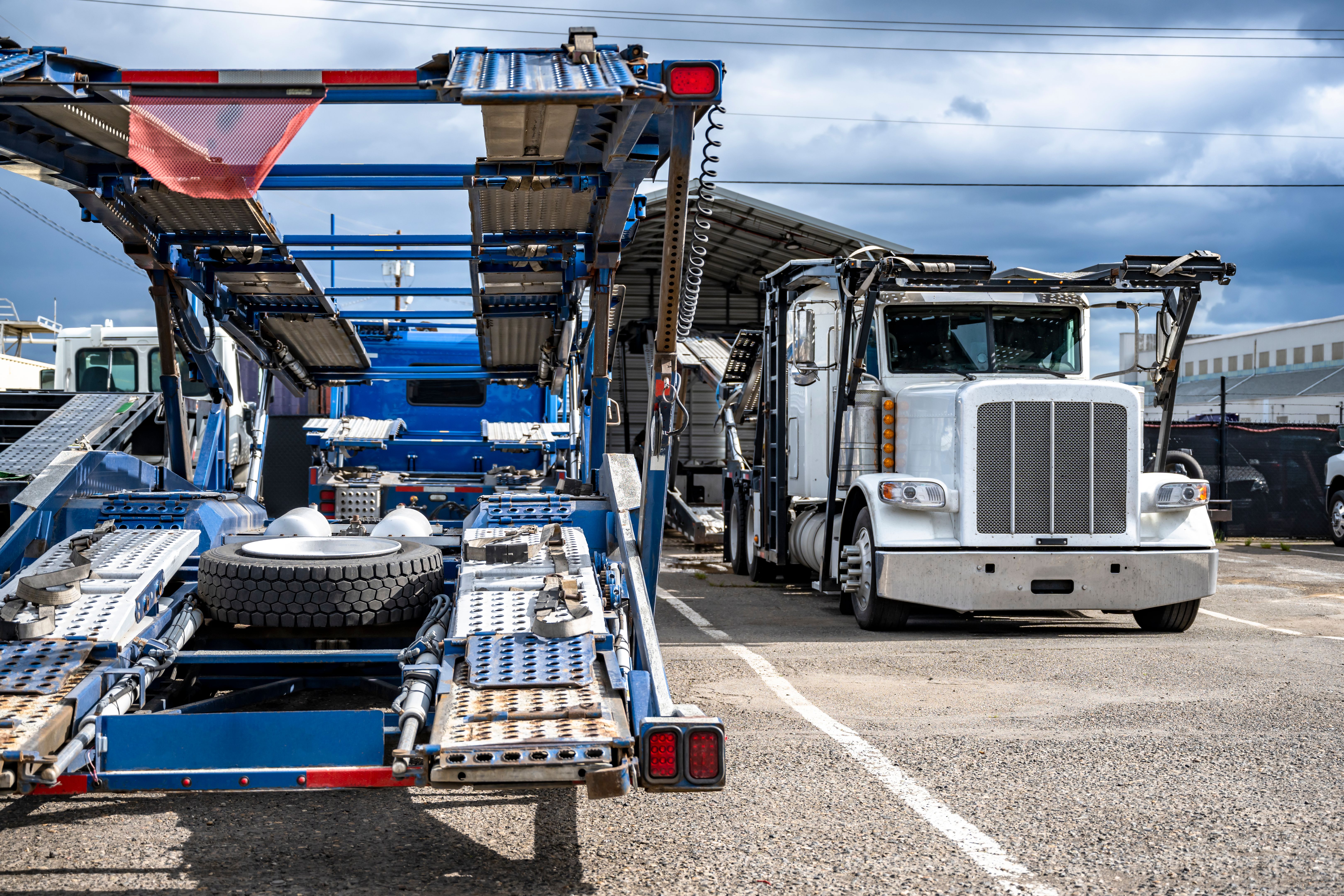 Professional big rig semi trucks with empty car hauler semi trailers standing on the industrial parking lot waiting for the next cars load
