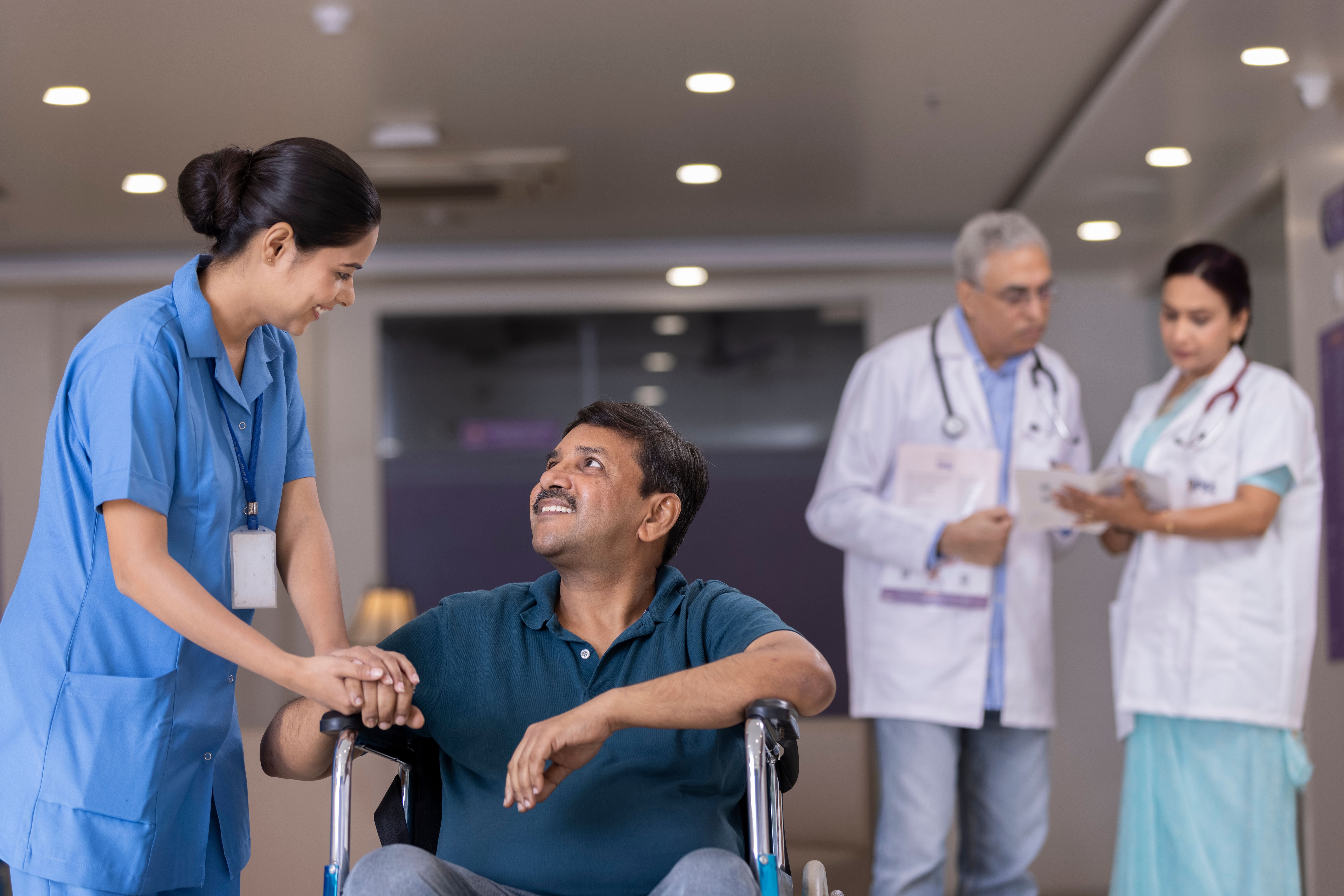 Nurse talking to disabled patient while doctors discussing in background at the hospital