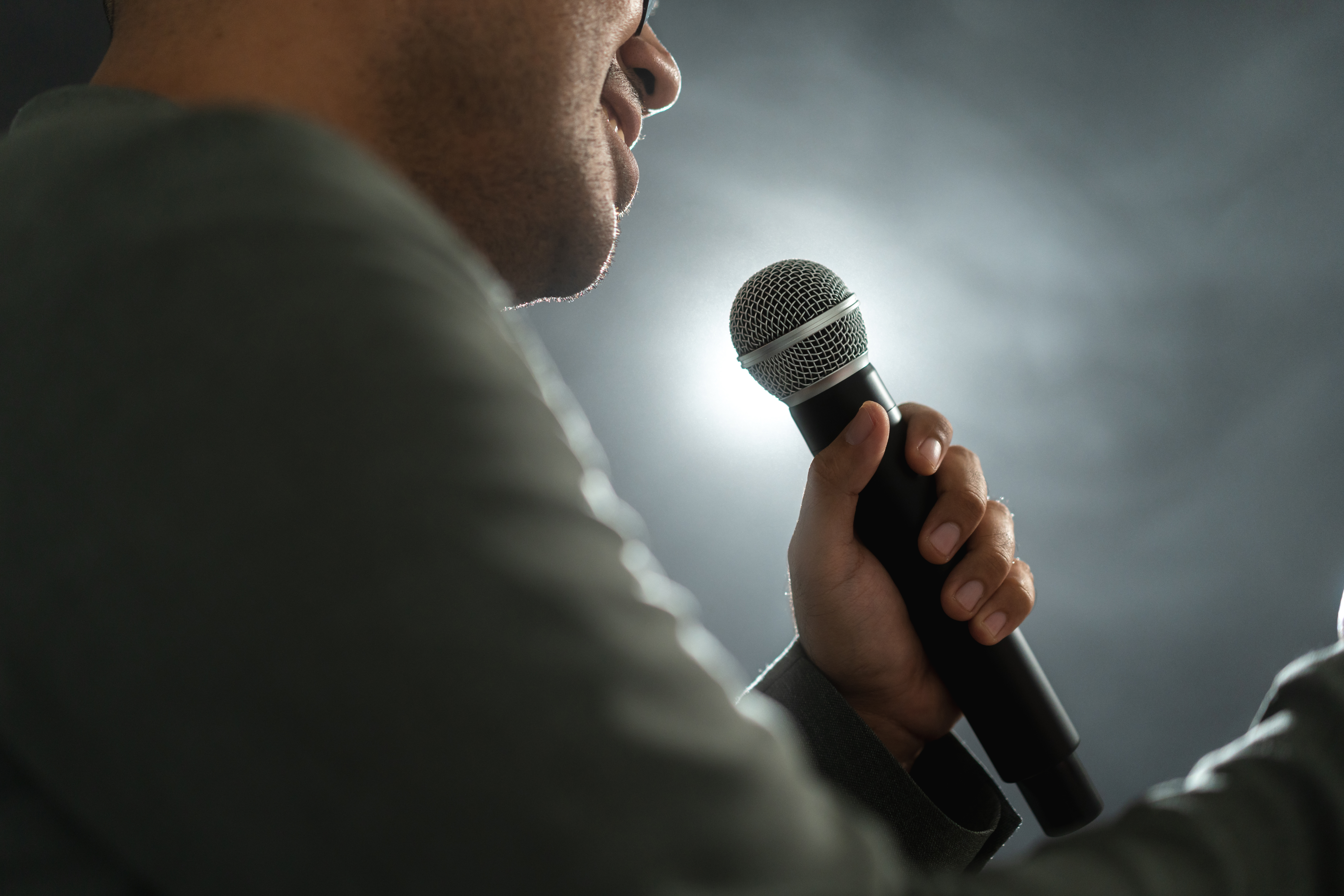 Confident successful speaker man talking on stage with spotlight strike through the darkness at corporate business event. Public speaker giving talk at conference hall. Stand up comedian.