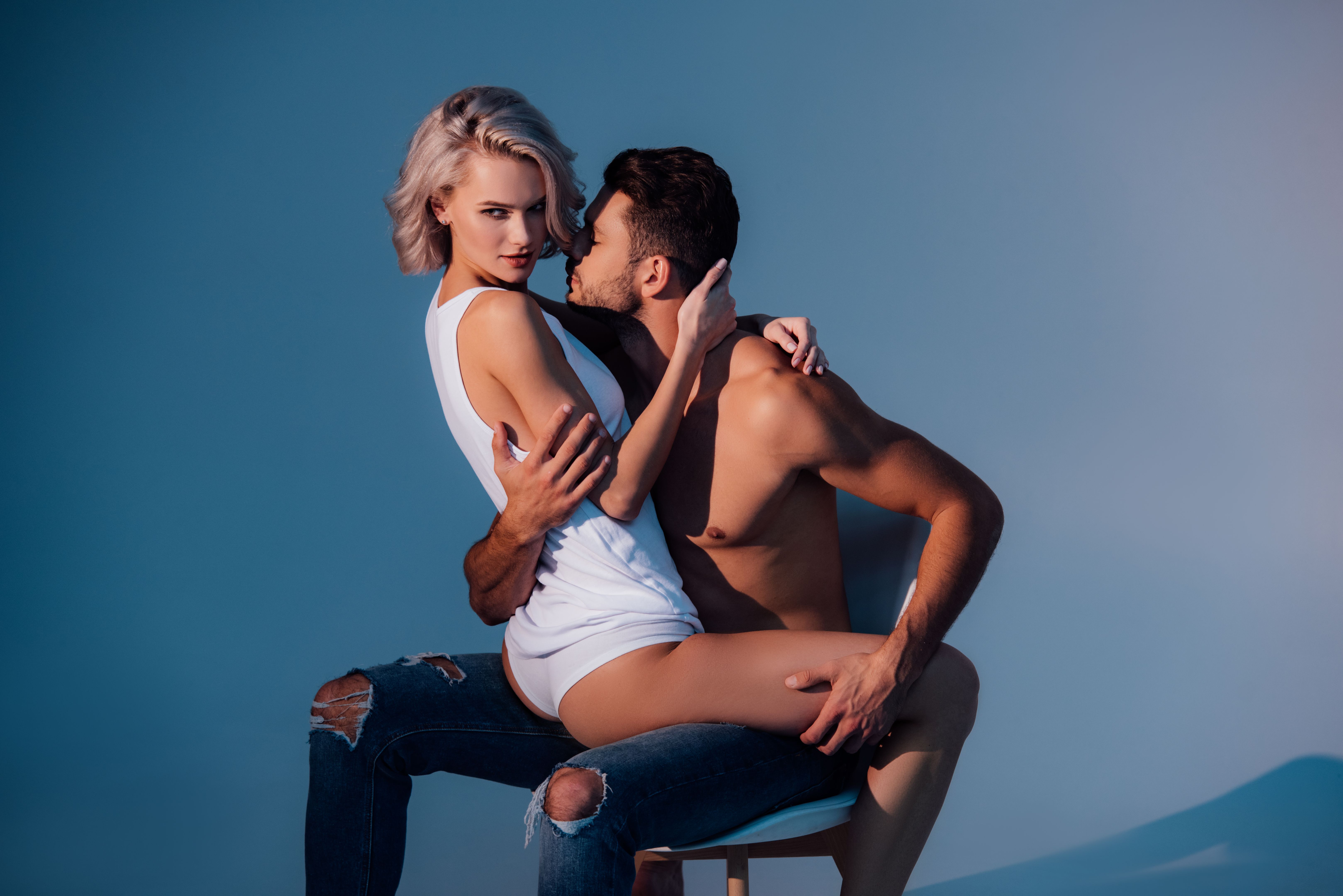 passionate heterosexual couple sitting on chair and hugging on dark blue background