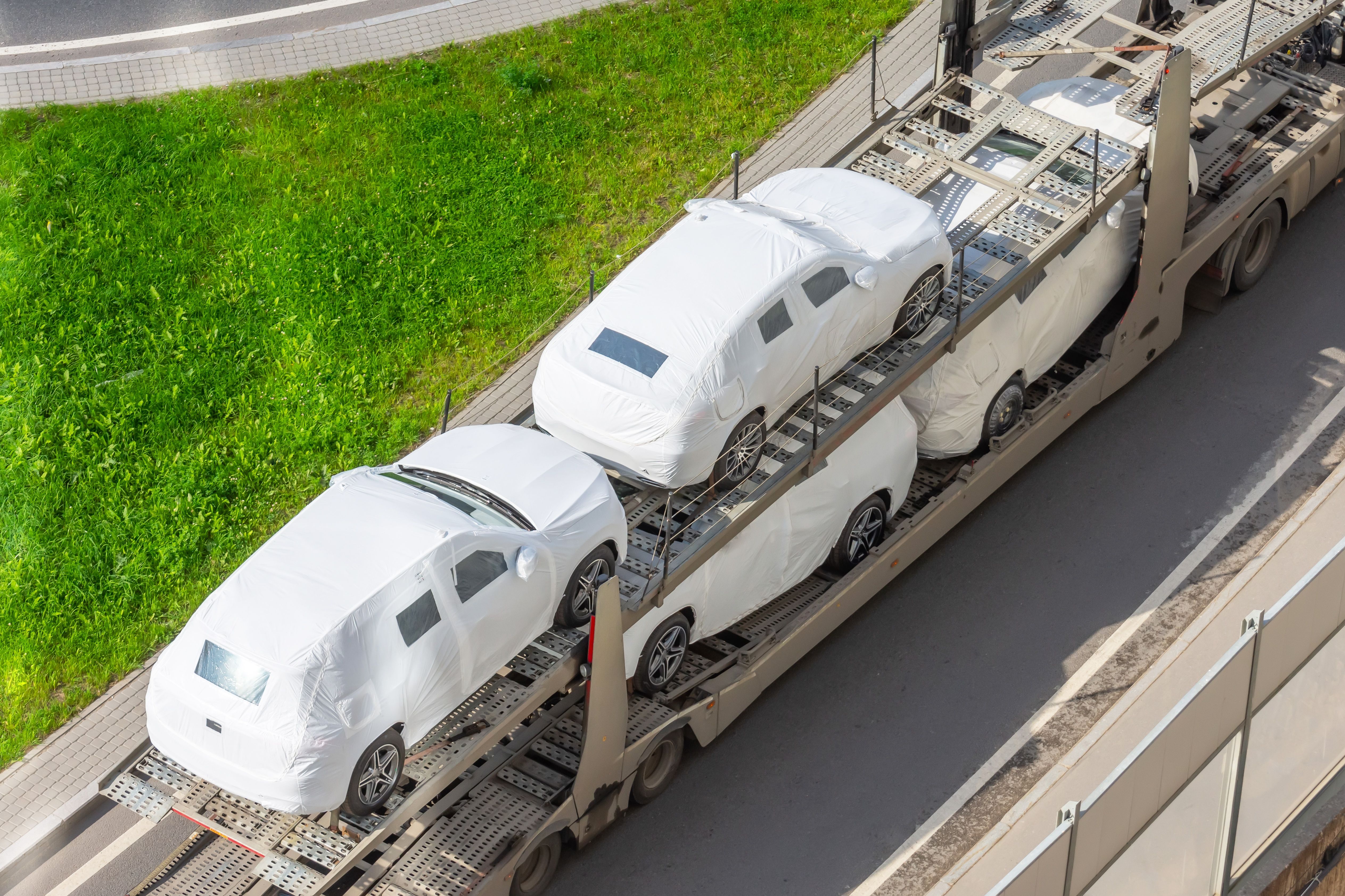 Transportation of new cars covered with protective fabric tarp on a truck trailer.