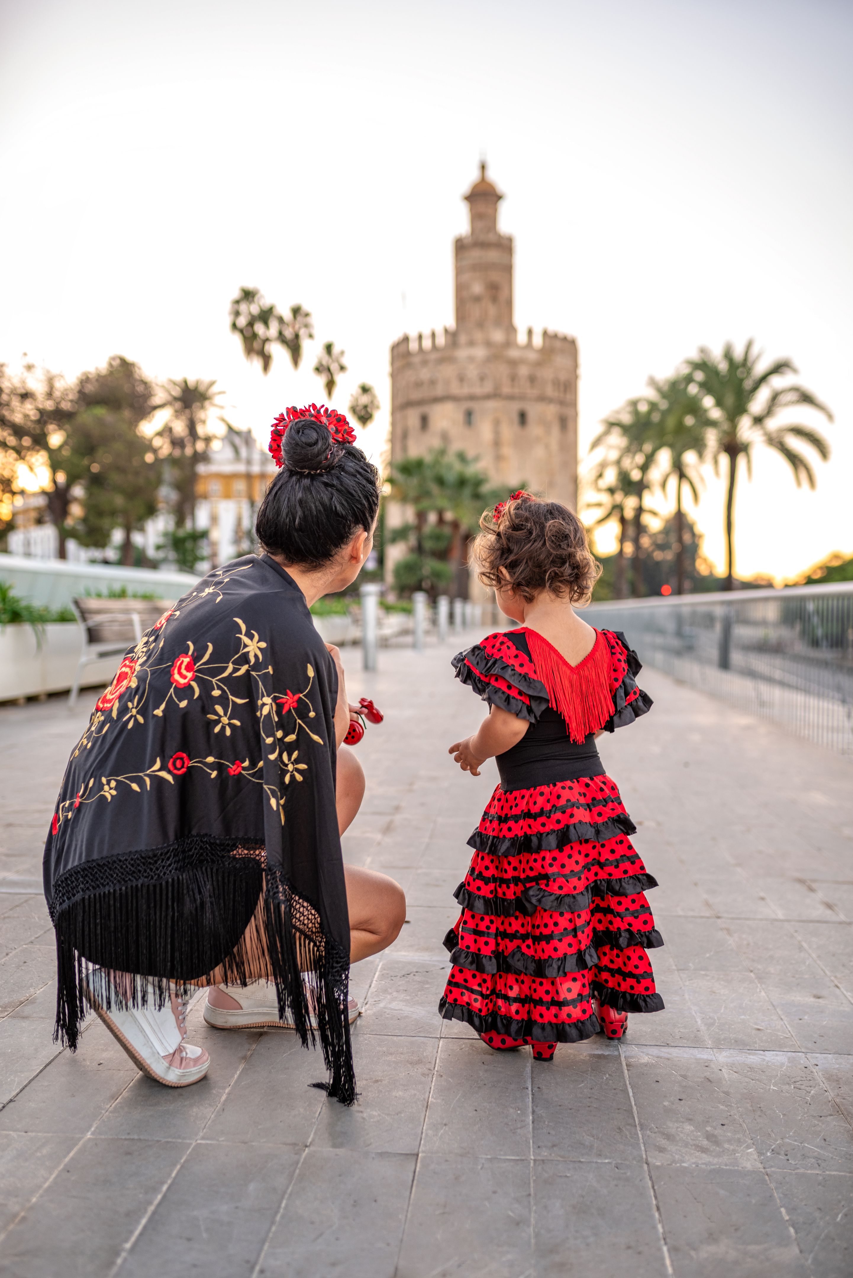 mother and young daughter dressed in flamenco dress in front of the Torre del Oro in Seville