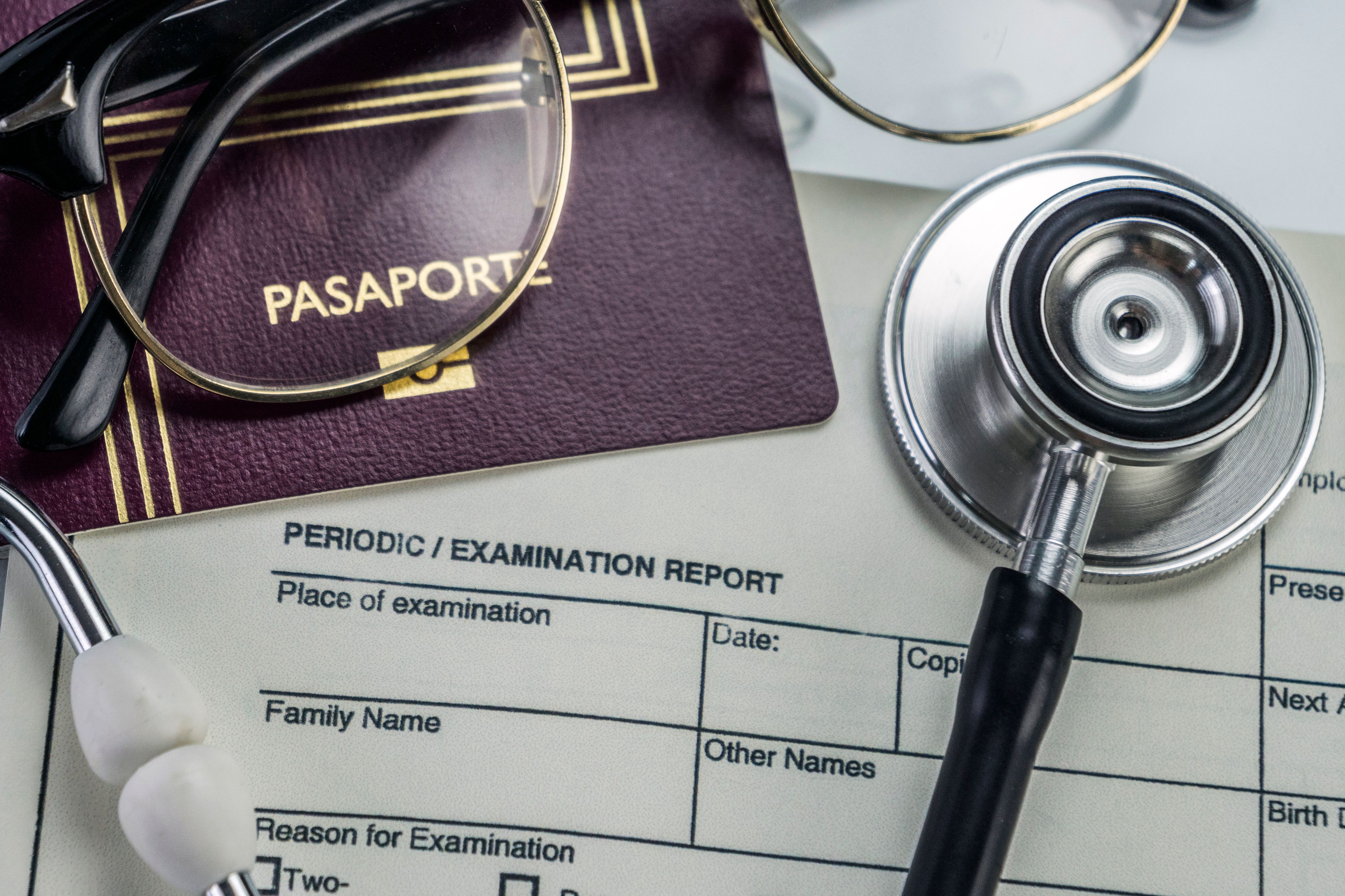Close-up of a passport, stethoscope, and medical examination form symbolizing health checks before travel.