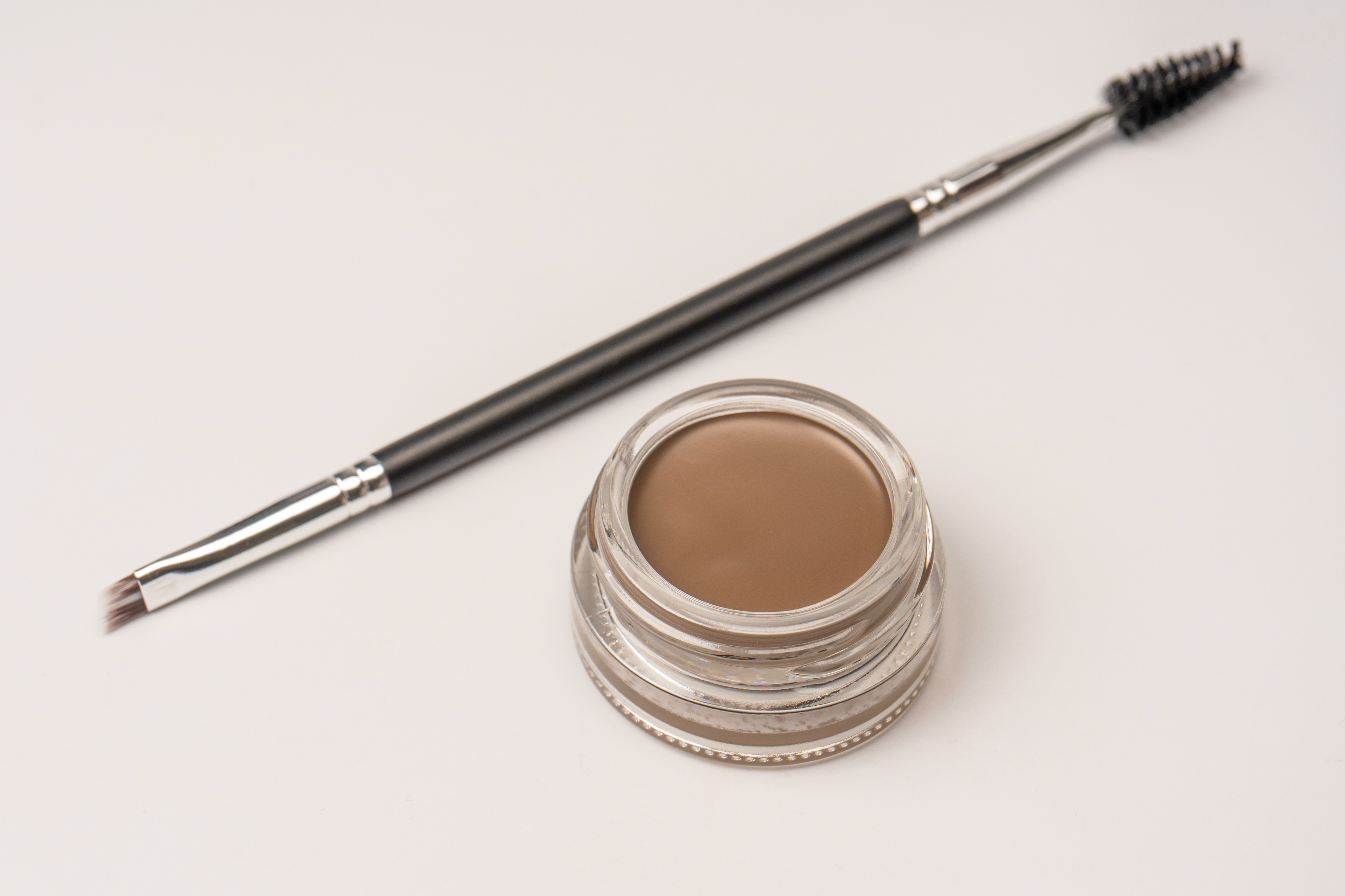 A brow pomade in blonde shade with brush isolated on a white background.