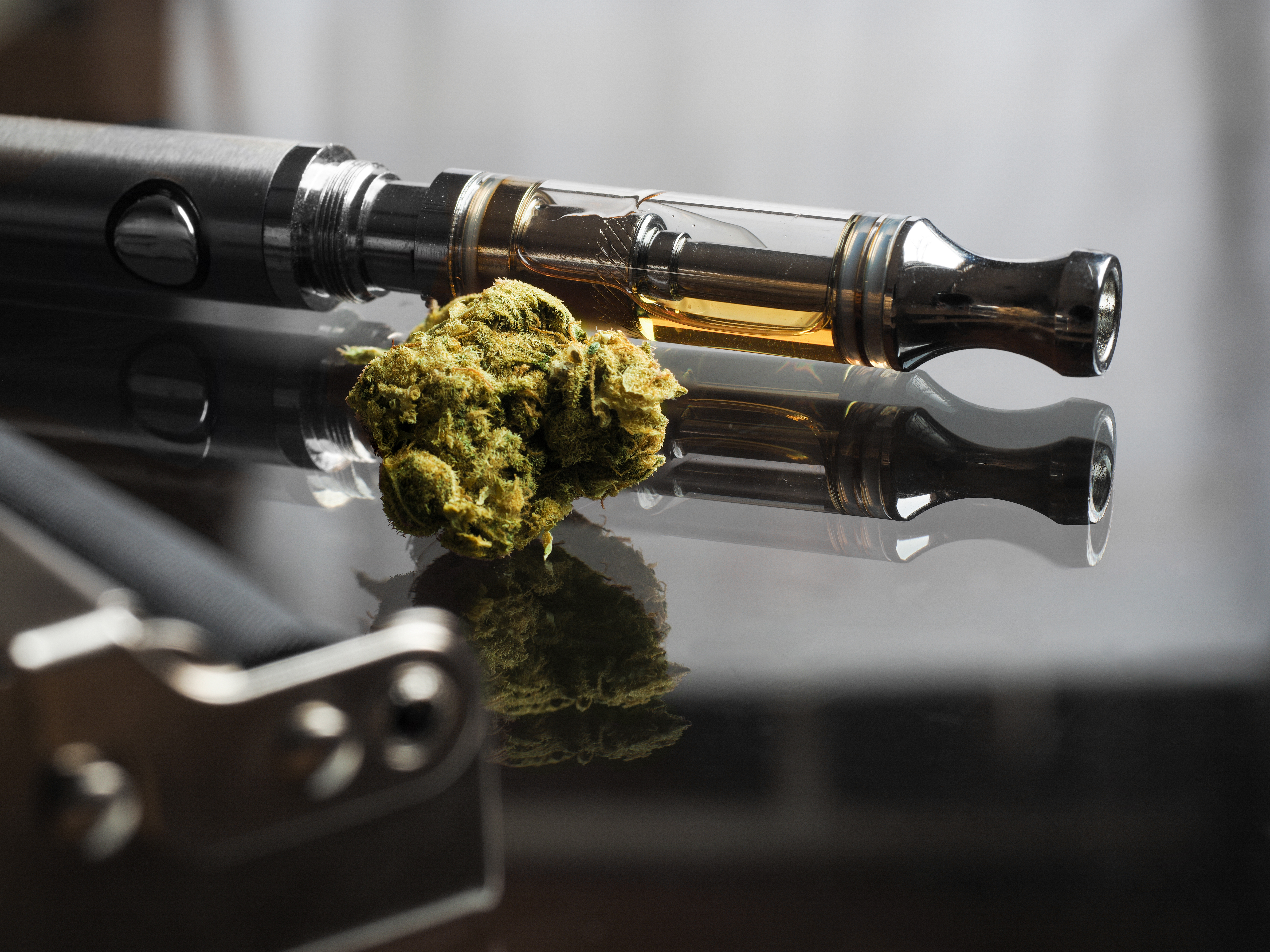 Close up shot of real cannabis or weed with cannabis oil in cartridge of vape  pen in the background, roller blurred in foreground and text space on the right under the dark theme