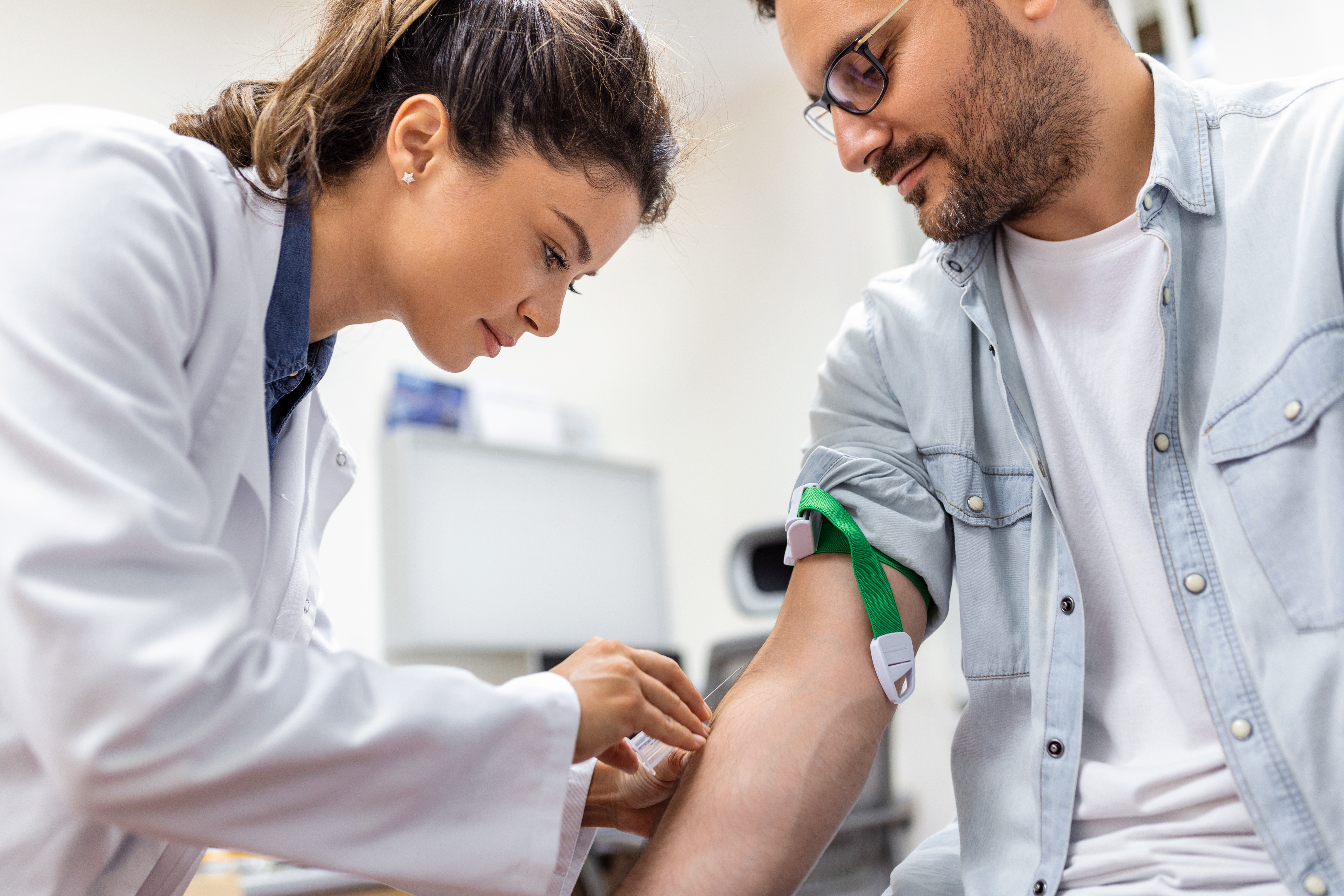 Friendly hospital phlebotomist collecting blood sample from patient in lab. Preparation for blood test by female doctor medical uniform on the table in white bright room Friendly hospital phlebotomist collecting blood sample from patient in lab. Preparation for blood test by female doctor medical uniform on the table in white bright room