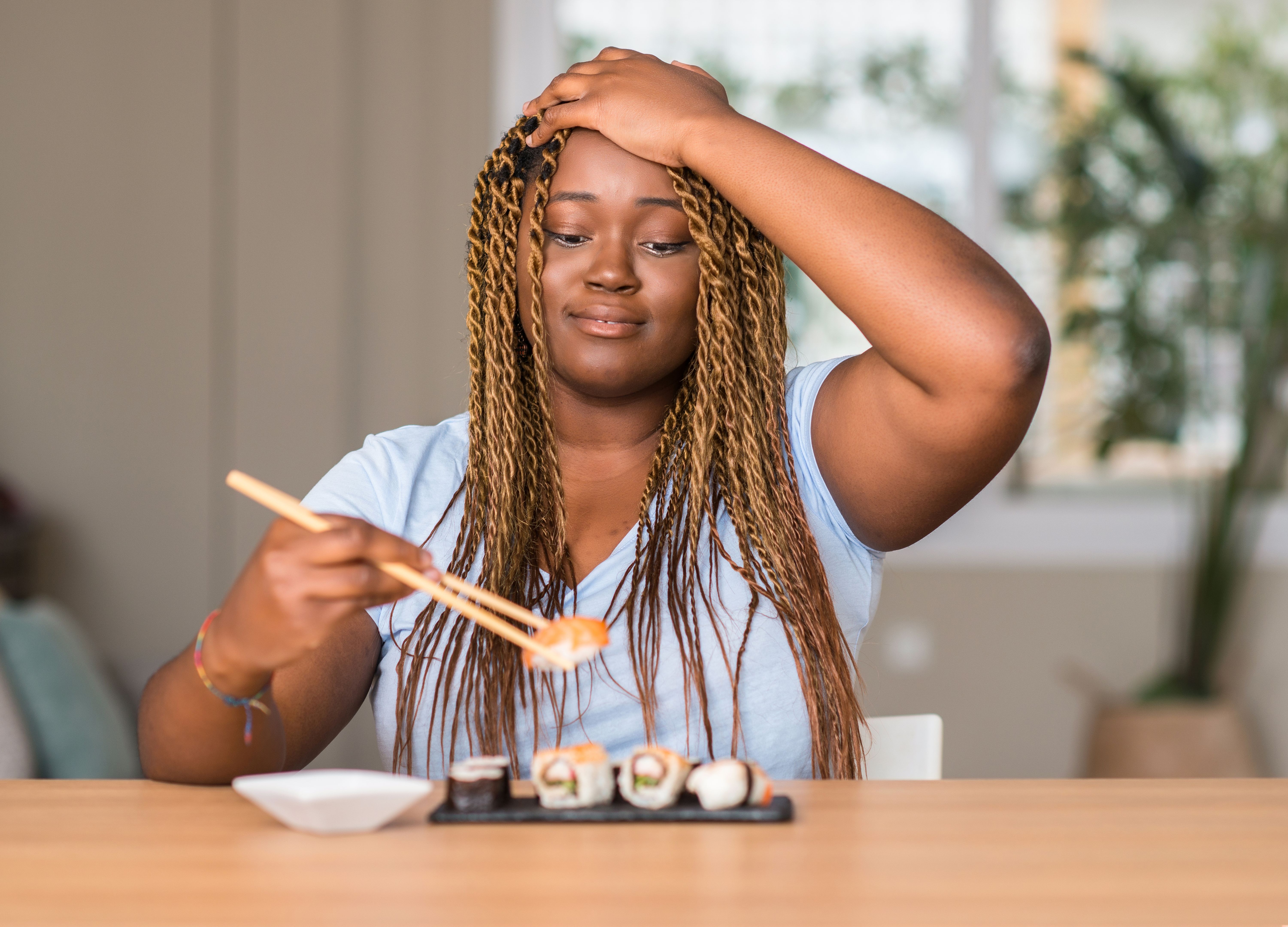 African american woman eating sushi stressed with hand on head, shocked with shame and surprise face, angry and frustrated. Fear and upset for mistake.