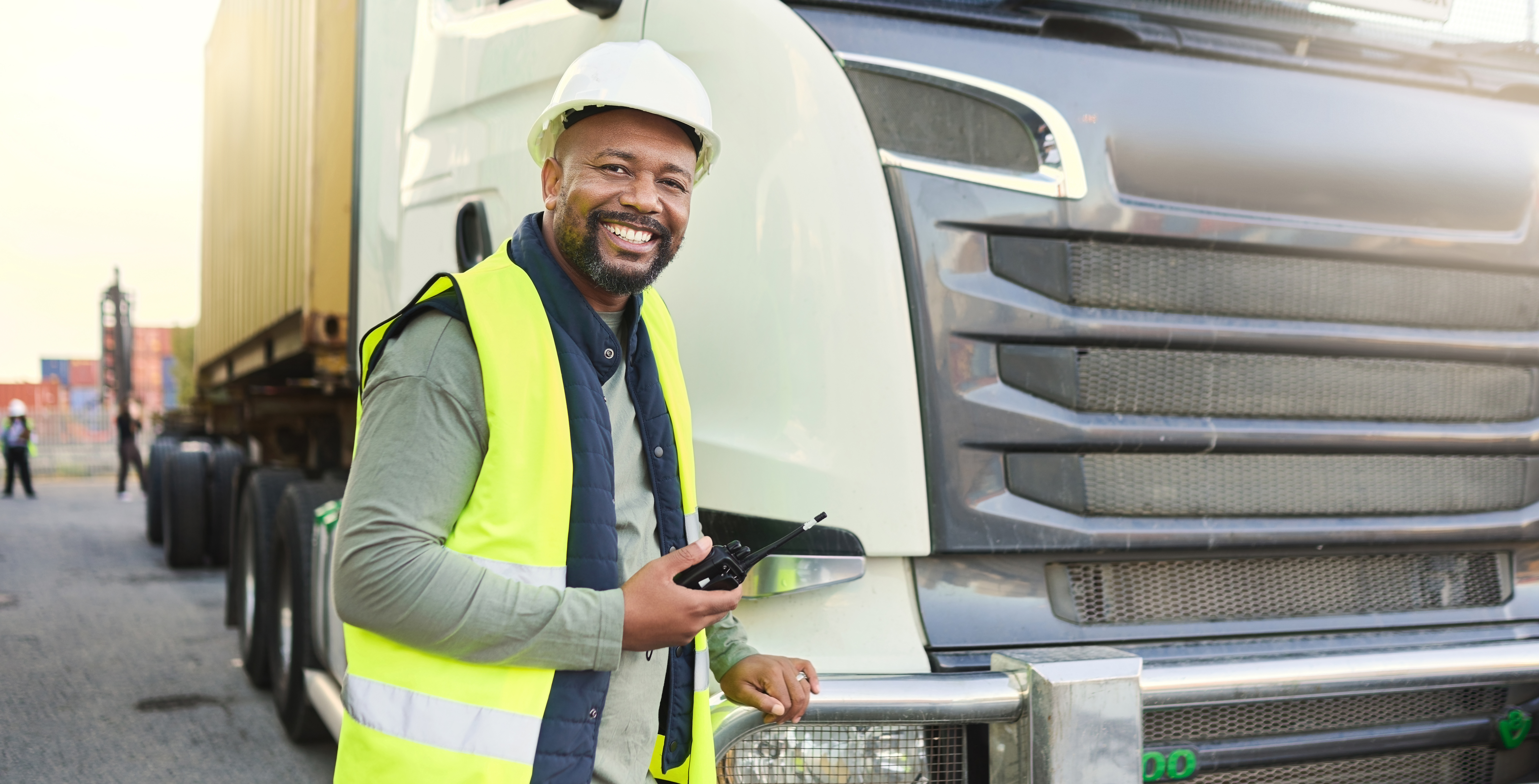 Construction worker in shipping business by delivery truck in shipyard. Black man truck driver with walkie talkie doing logistics, transport and export of cargo container in distribution industry Construction worker in shipping business by delivery truck in shipyard. Black man truck driver with walkie talkie doing logistics, transport and export of cargo container in distribution industry