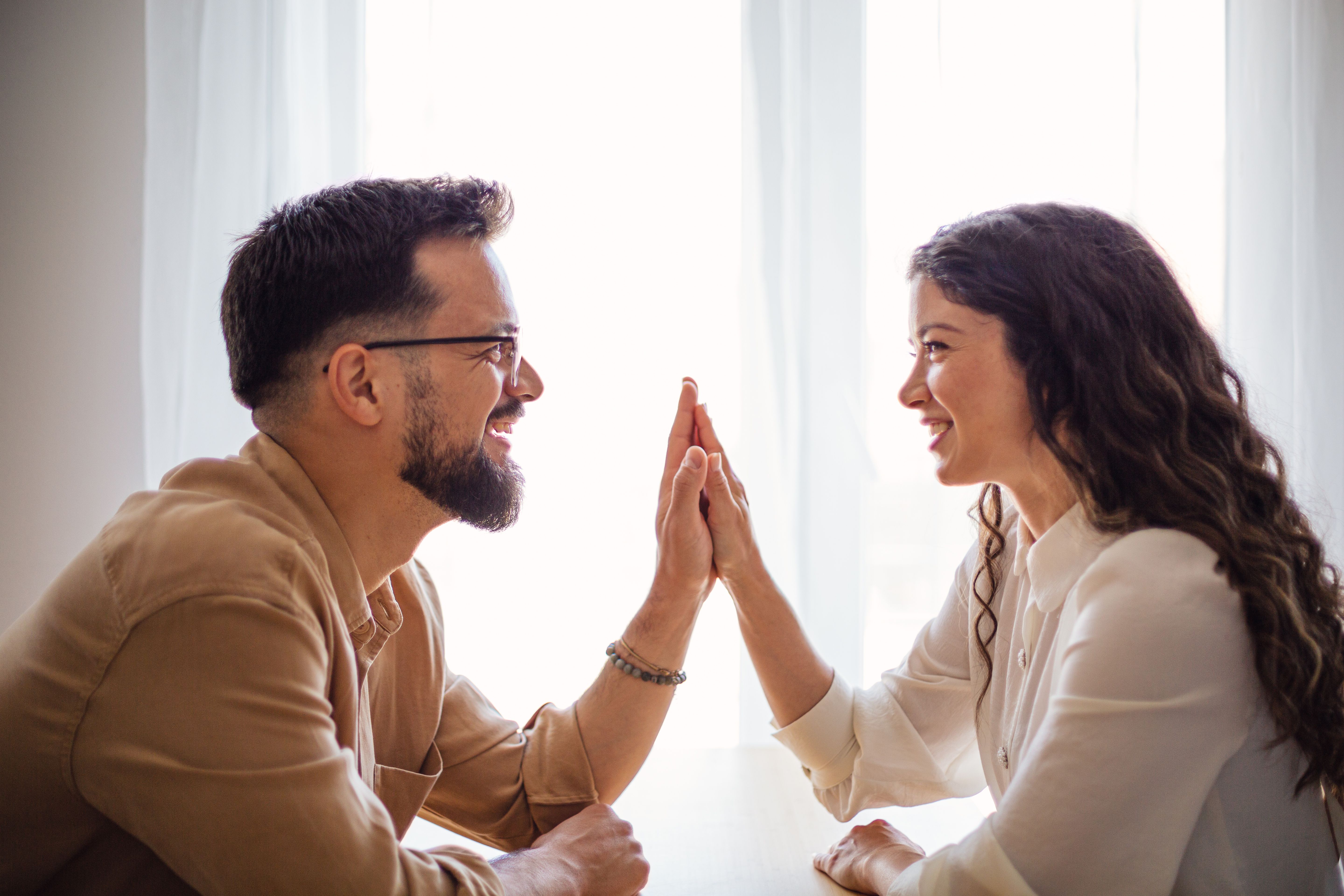 Young couple joining hands, celebrating a success at home