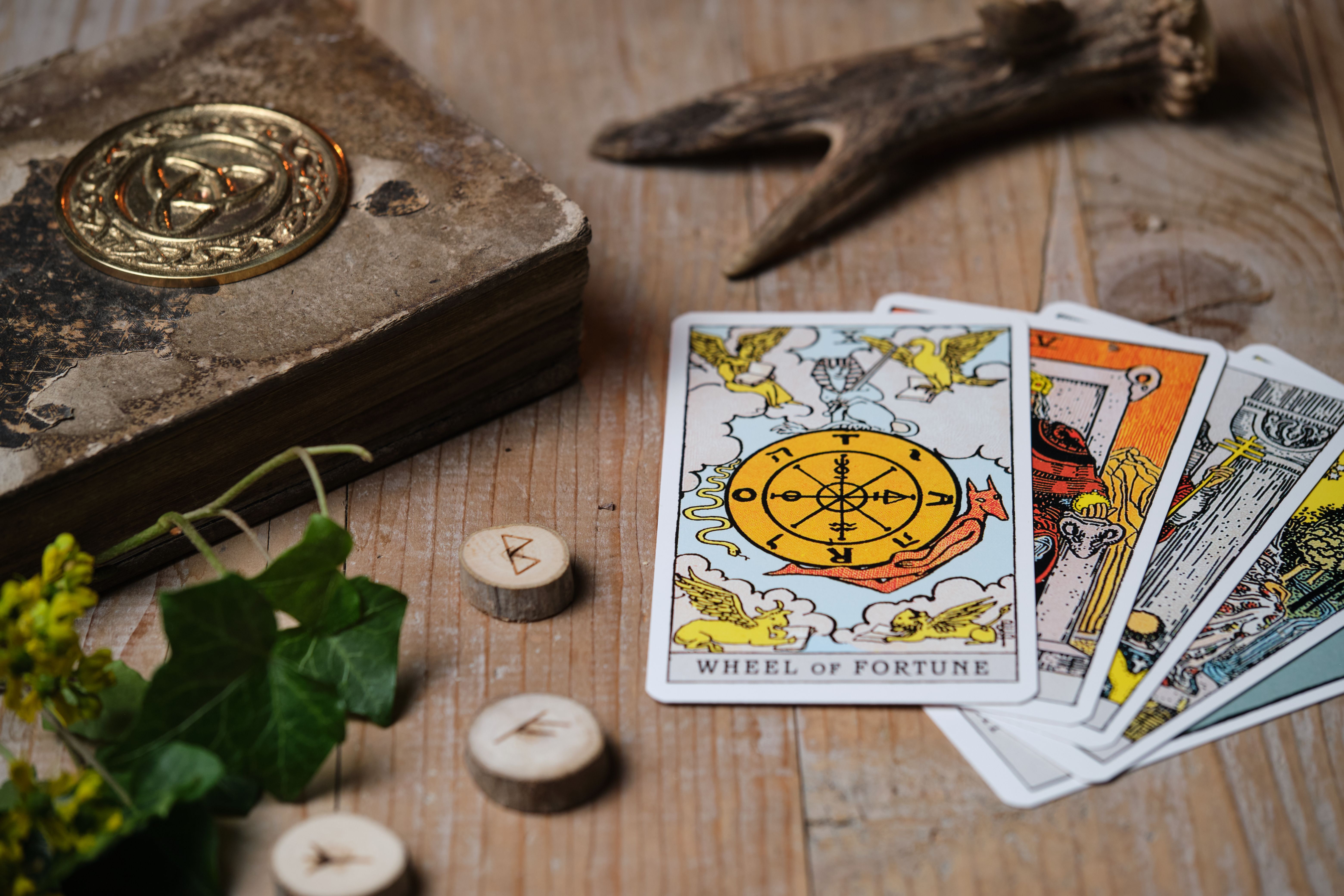 Tarot cards and runes on an old wooden table, "Wheel of Fortune" card placed on top – moody mystic scene