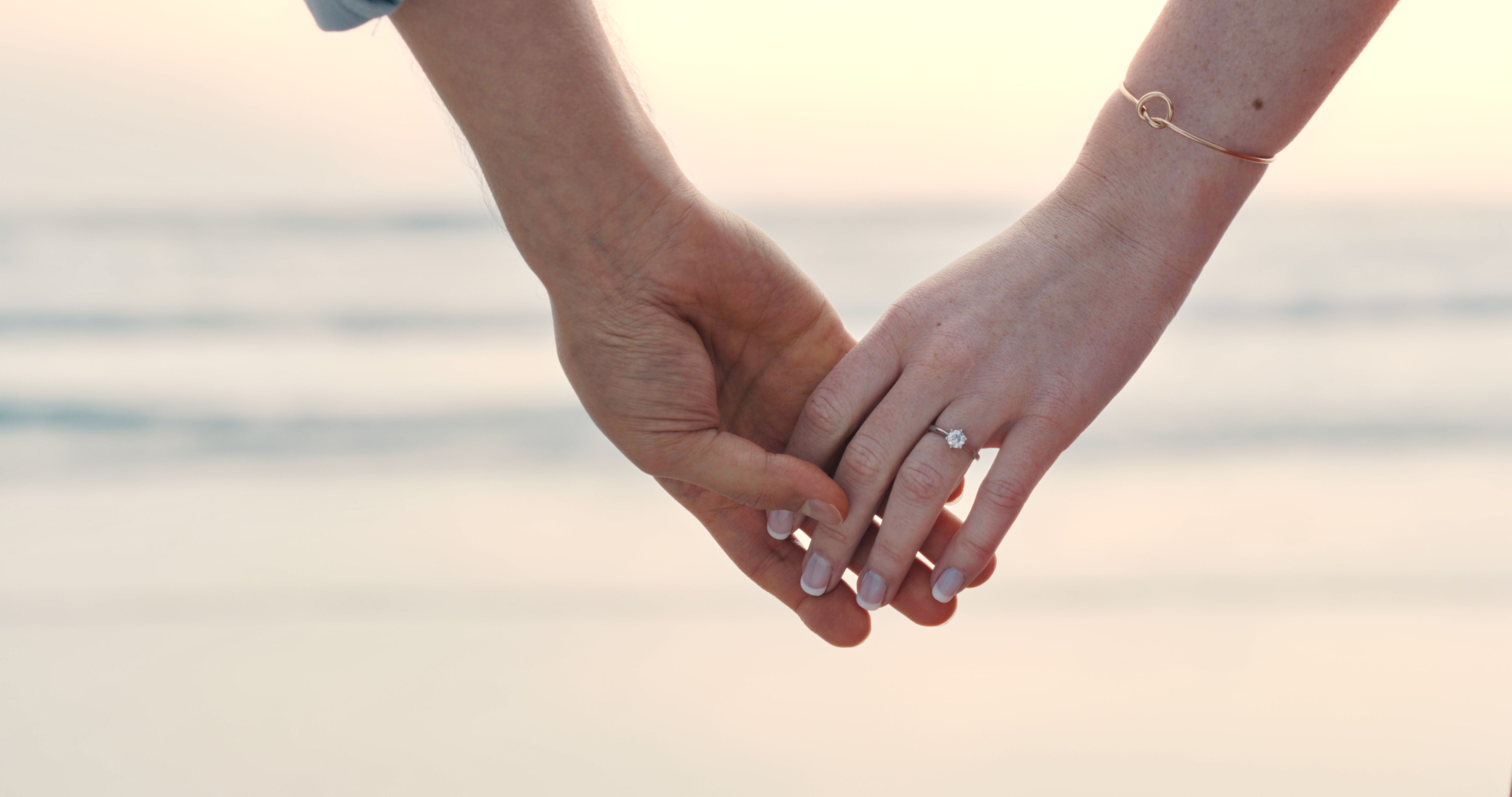 An unrecognizable couple holding hands and wearing an engagement ring. Closeup of a man and woman after their proposal at the beach An unrecognizable couple holding hands and wearing an engagement ring. Closeup of a man and woman after their proposal at the beach