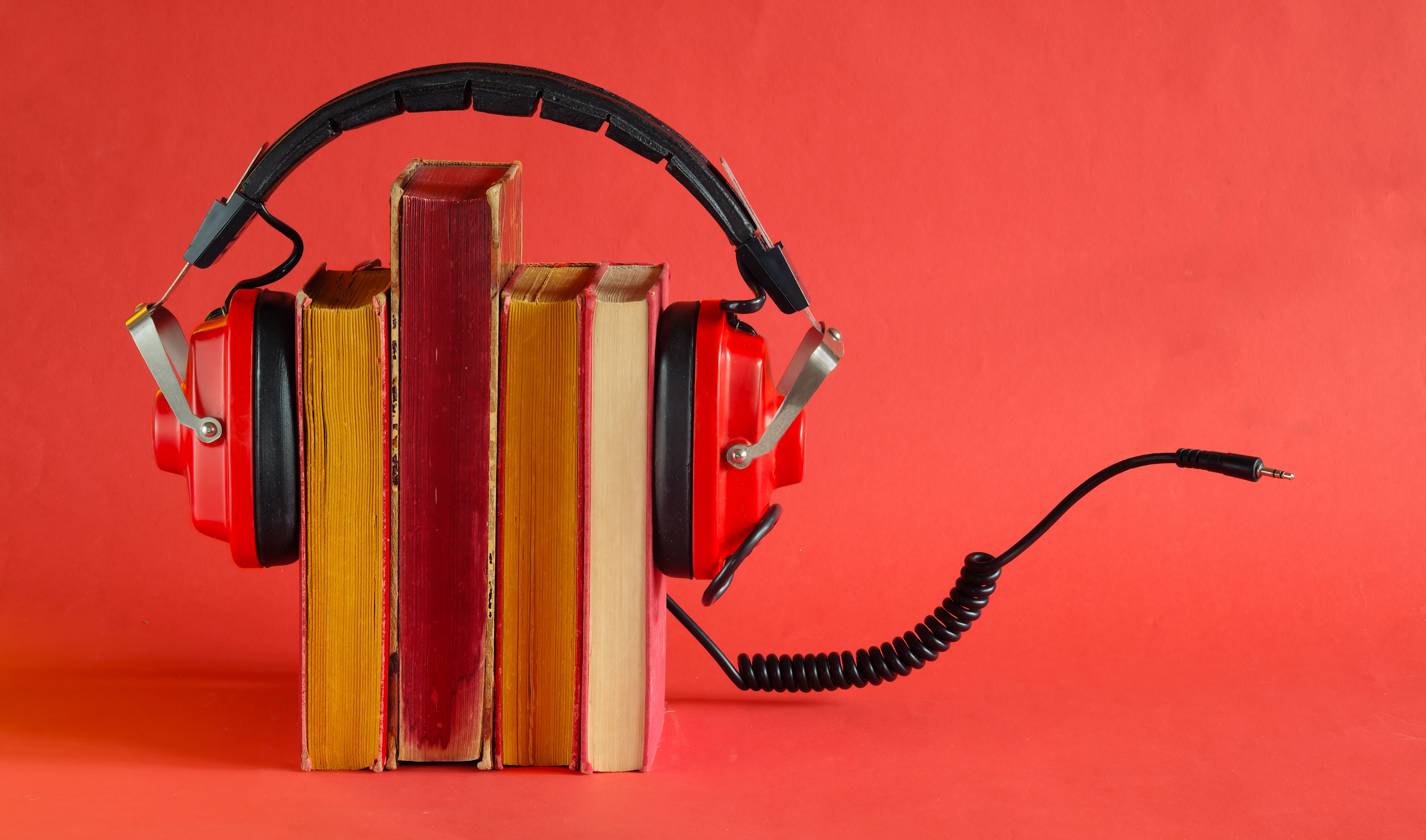 audio book concept with row of books,and vintage headphones, cable and audio plug, red background, free copy space