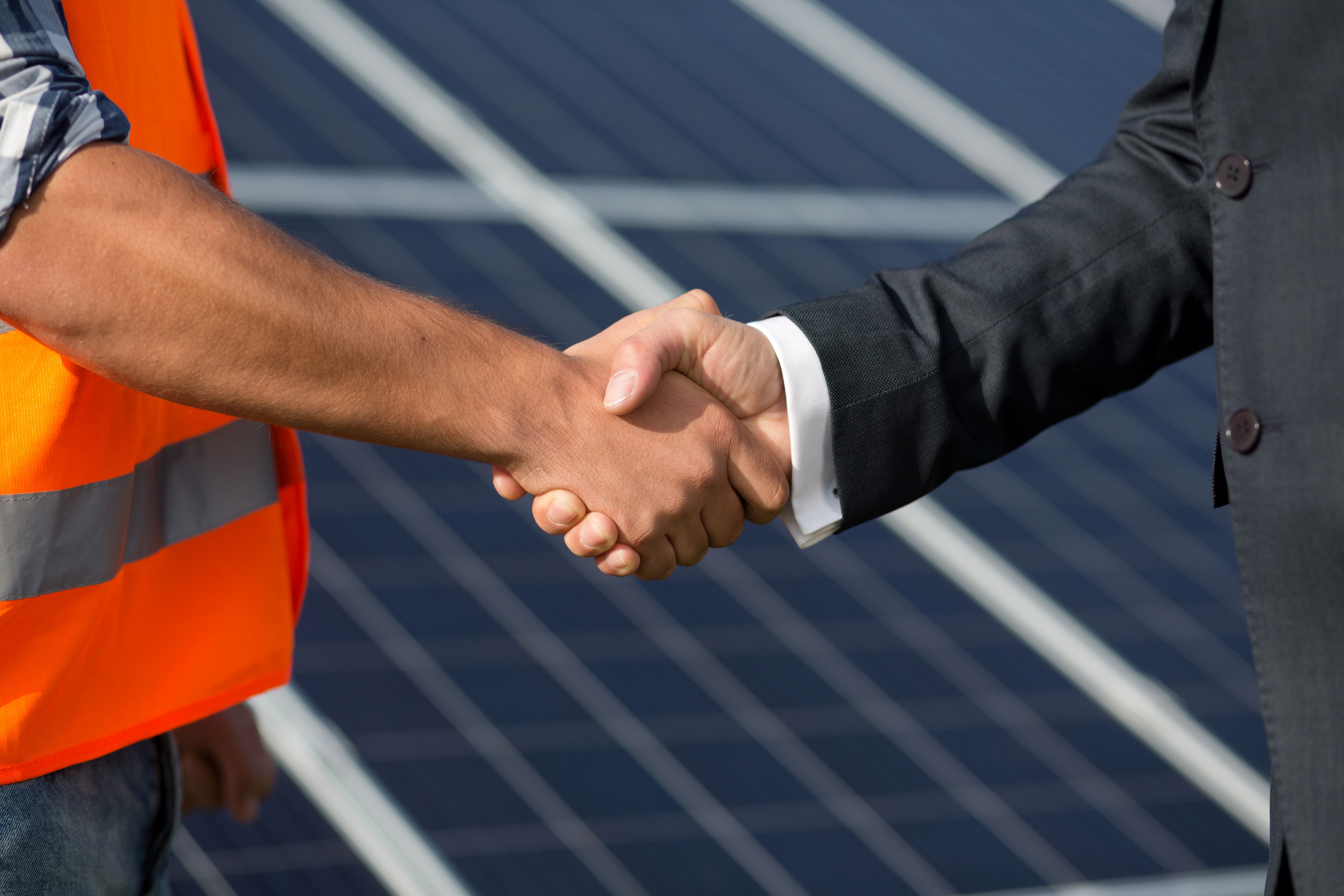 Foreman and businessman shaking hands at solar energy station.